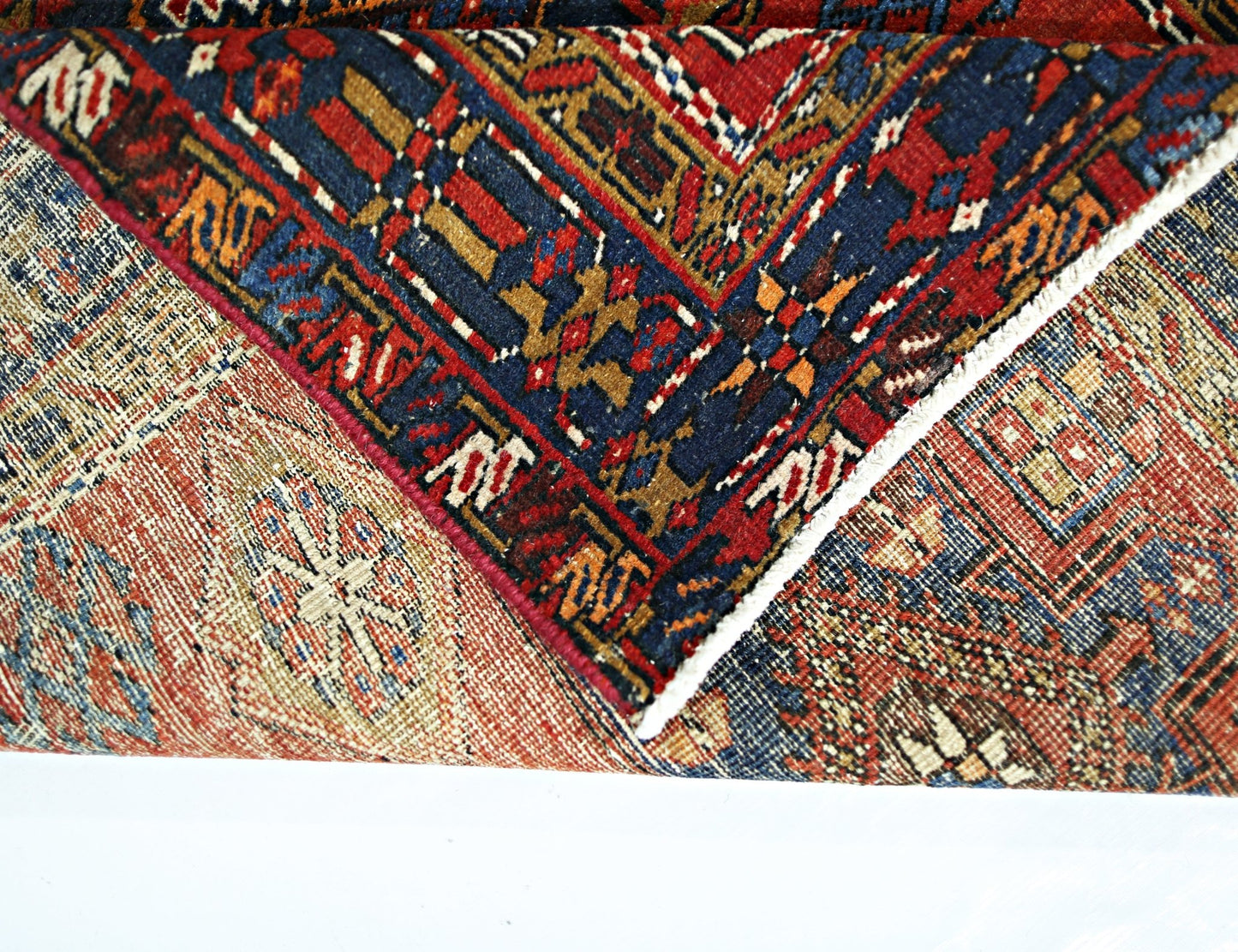 A folded vintage Persian runner featuring intricate geometric patterns in red, blue, and tan.