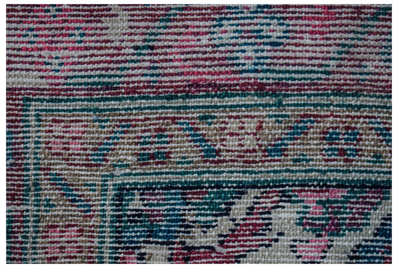 A close-up of a vintage Persian Hamadan runner featuring intricate patterns in pink, blue, and tan.