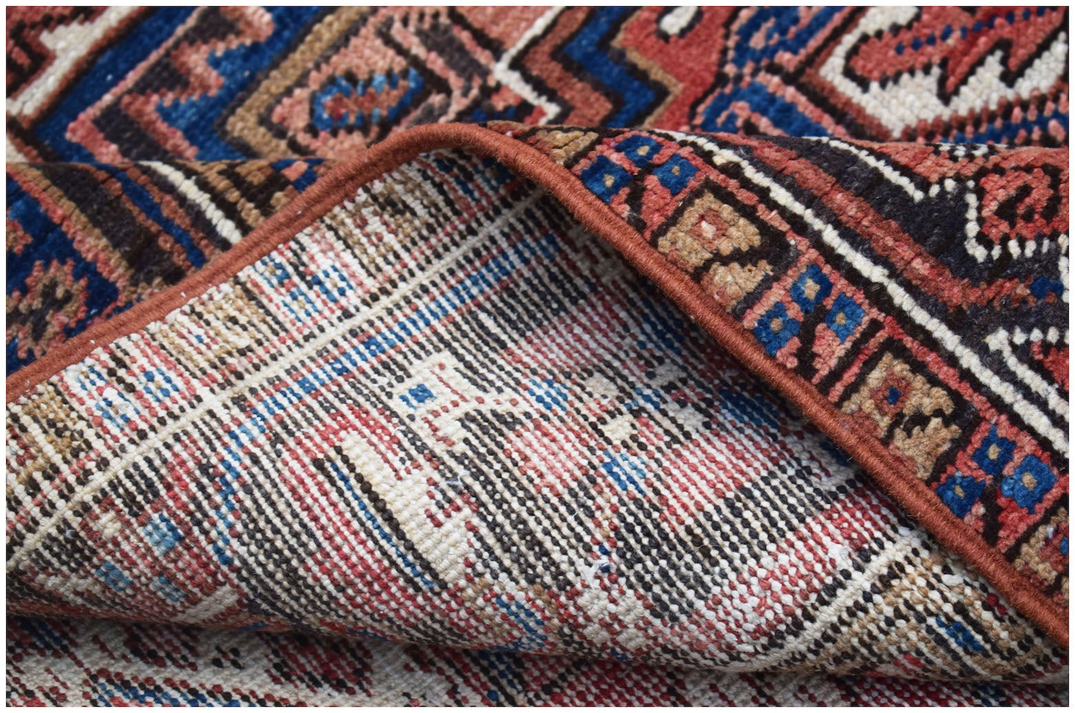 A corner of a vintage Persian Heriz rug showing its handwoven wool pile and cotton foundation.