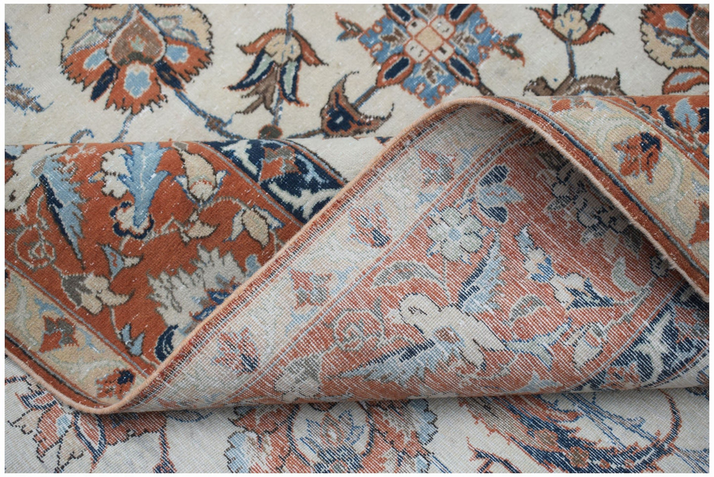 A vintage Persian Kashan rug featuring intricate floral patterns in rust, blue, and cream tones.