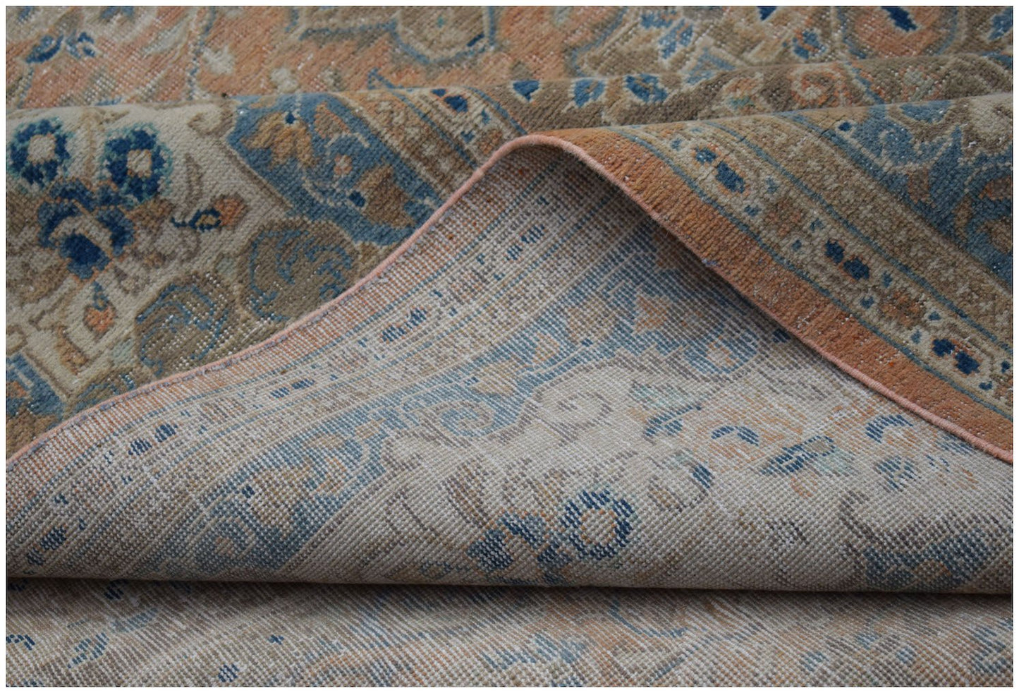A vintage Persian Kashan rug with a faded floral pattern in shades of blue, tan, and orange.