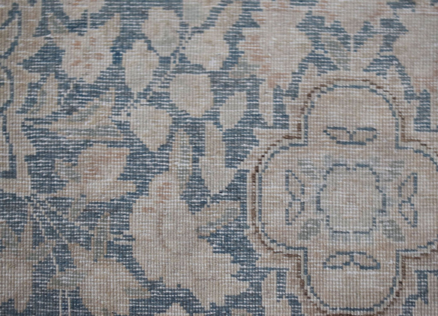 A close-up of a vintage Persian Kerman rug featuring intricate floral patterns in blue and beige.