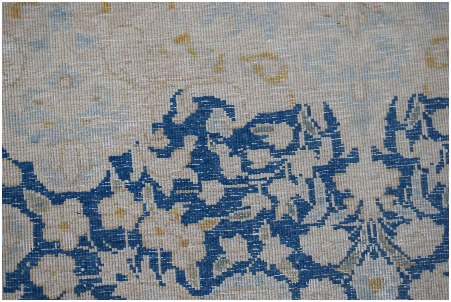 A close-up of a vintage Persian Kerman rug featuring intricate blue floral patterns on a cream base.