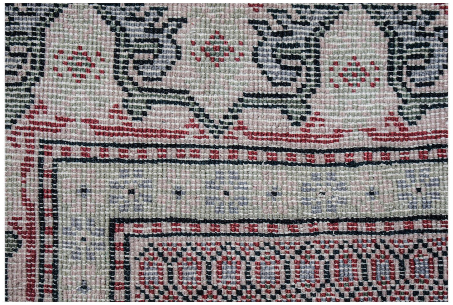 A close-up of a vintage Persian rug featuring intricate geometric patterns in pink, green, and black.