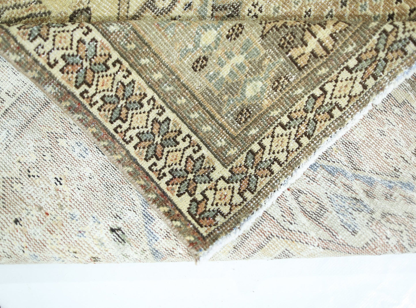 A corner of a vintage Persian Qashqai rug showing its intricate floral border and wool pile.