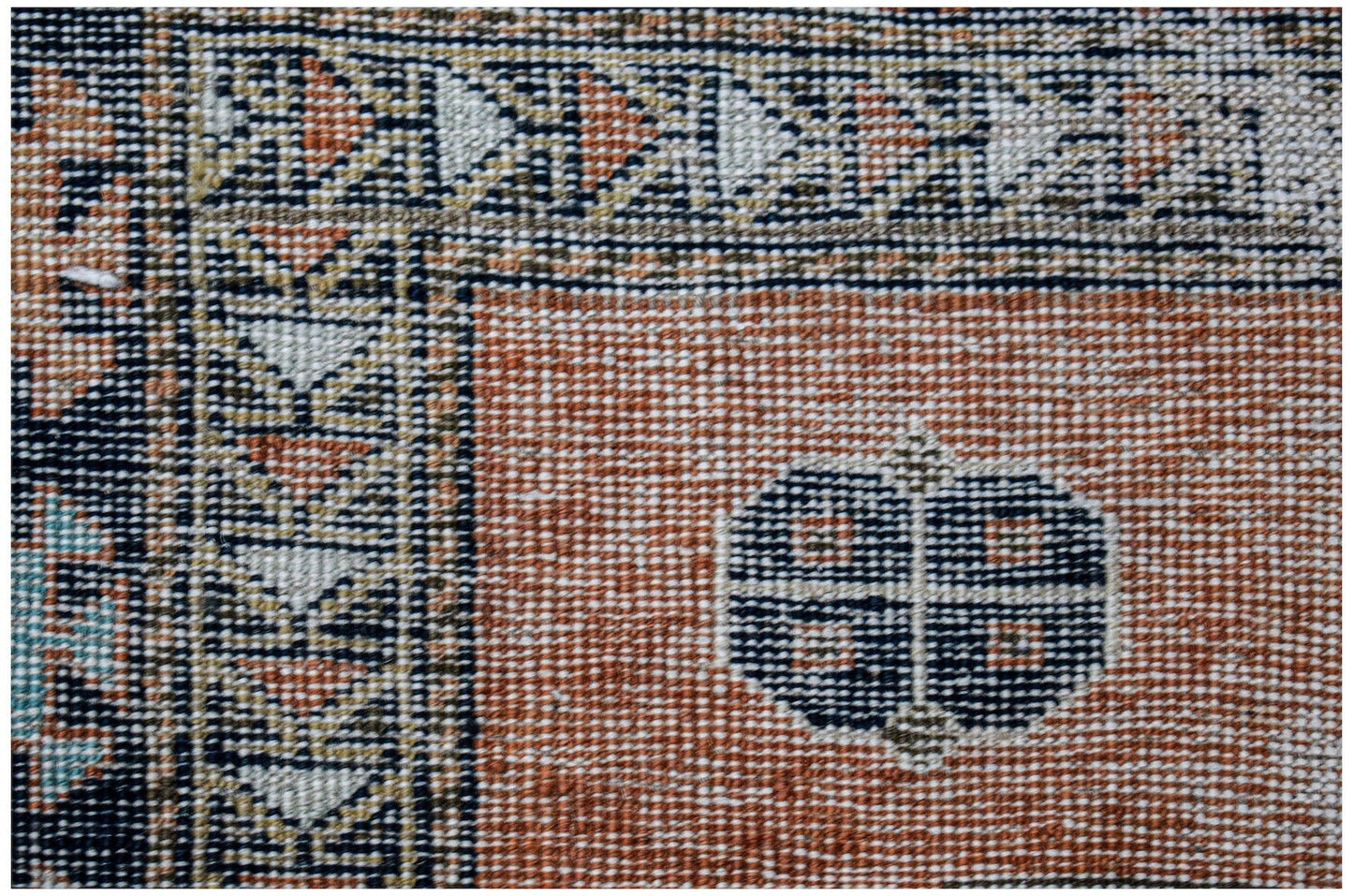 A close-up of a vintage Persian rug featuring a geometric border and a central floral motif.