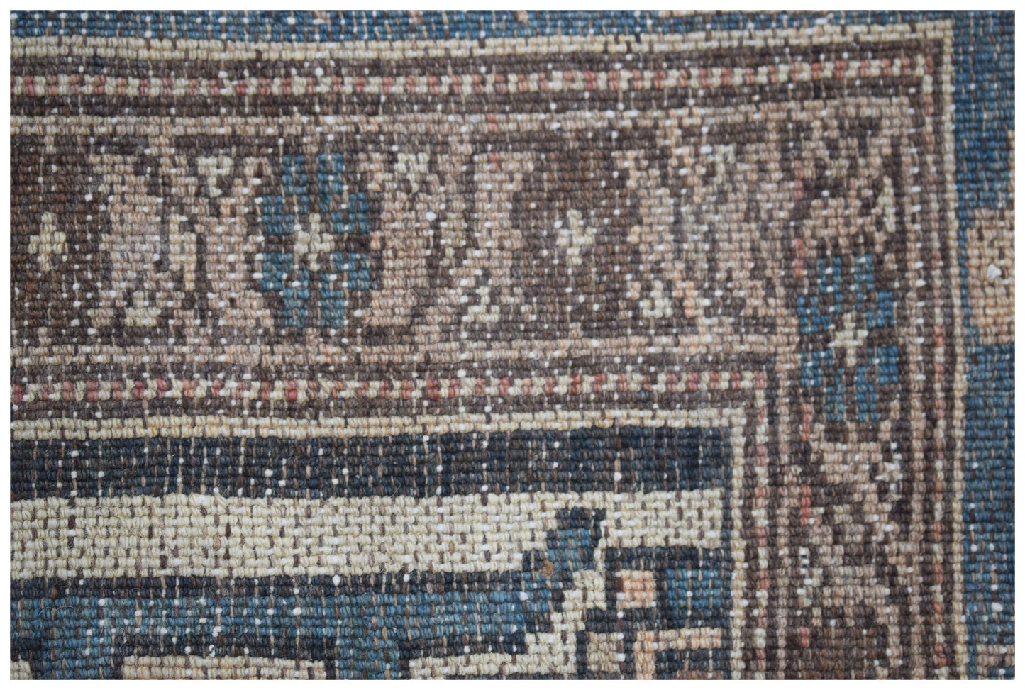 A close-up of a handwoven vintage Persian rug featuring geometric patterns in blue and brown tones.