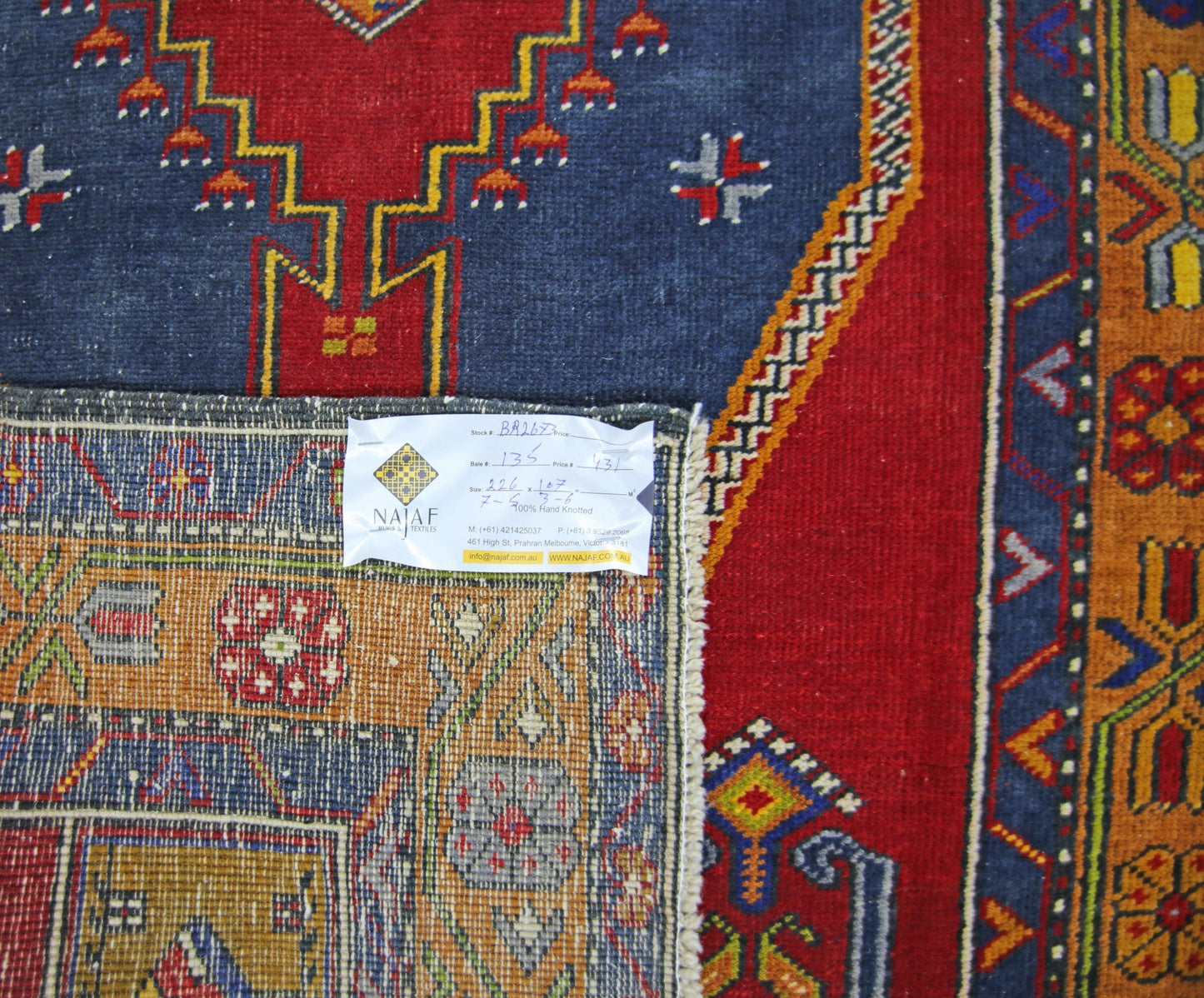 A vintage handmade Persian rug featuring geometric patterns in red, blue, and orange tones.