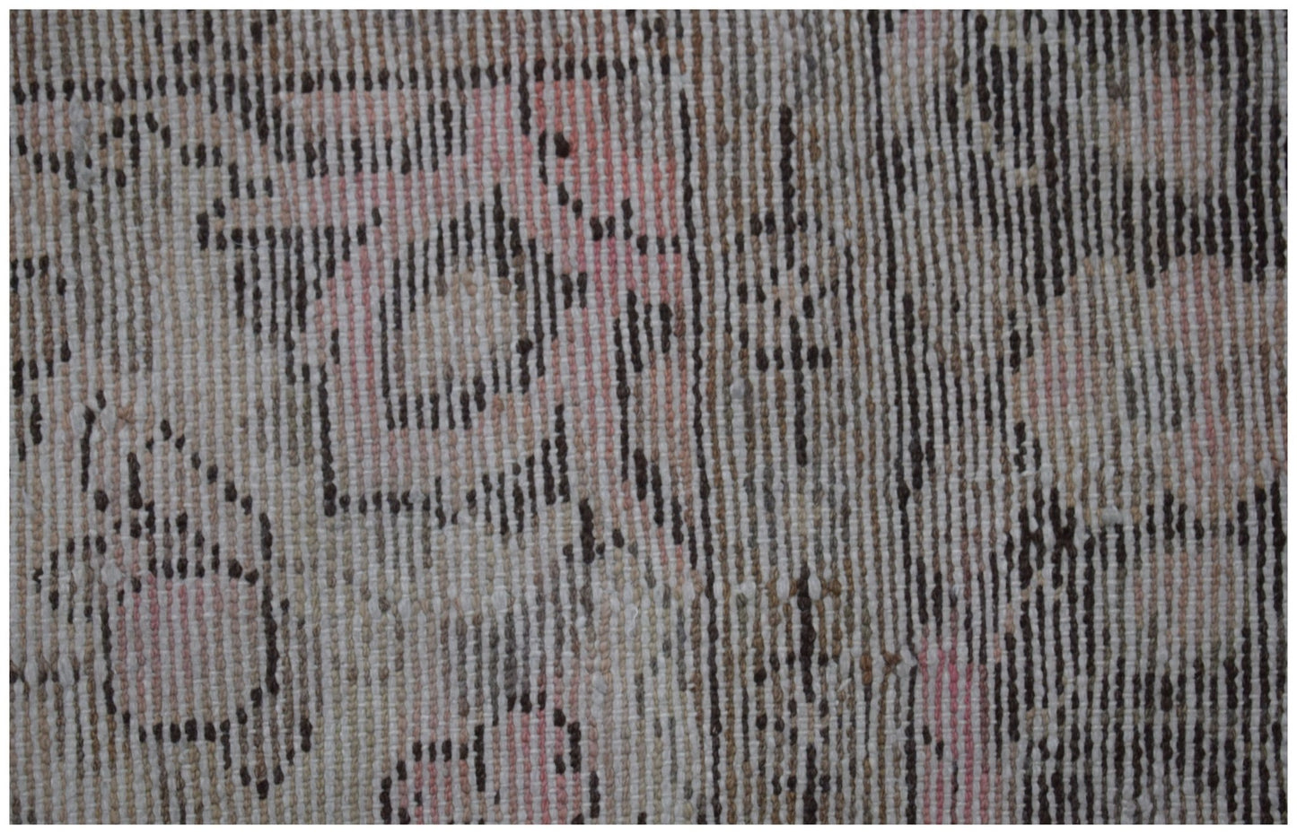A close-up of a vintage Persian rug featuring a faded geometric pattern in pink, brown, and cream.