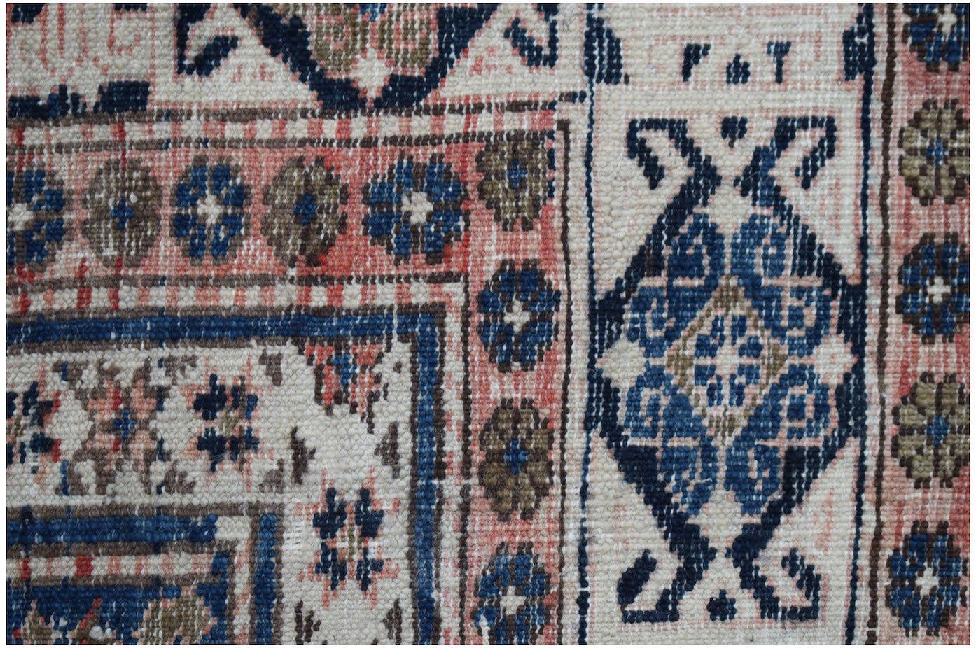A close-up of a vintage Persian rug featuring intricate geometric patterns in blue, pink, and tan.