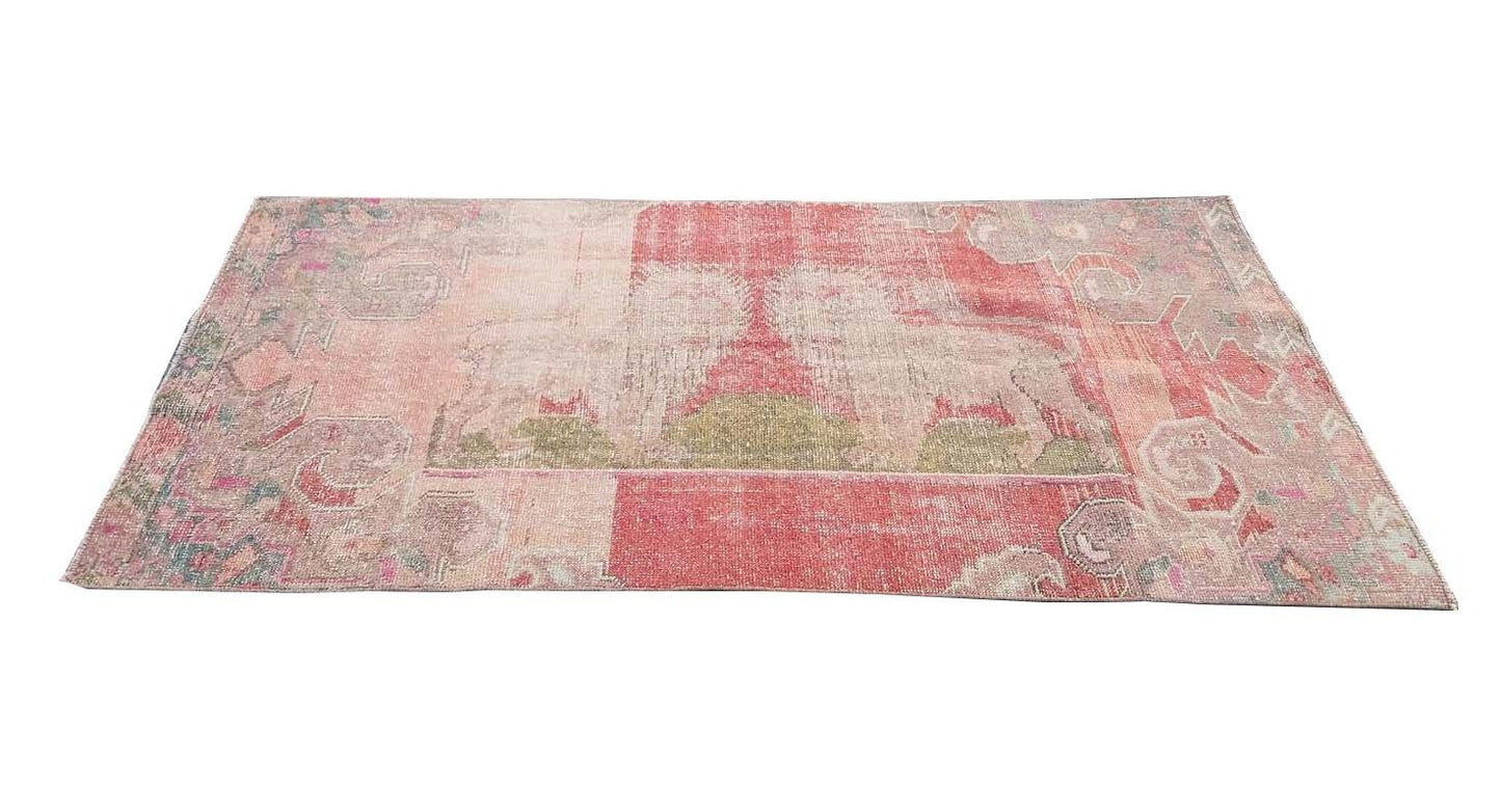 A rectangular vintage Turkish rug featuring a faded red and pink geometric pattern.