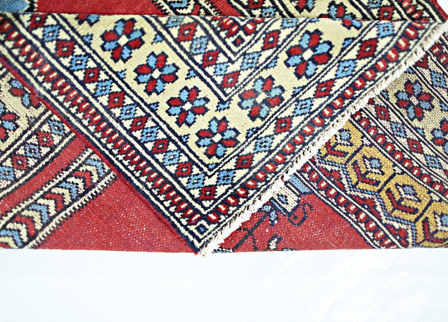 A folded vintage Turkish Kayseri rug featuring intricate geometric patterns in red, blue, and cream.