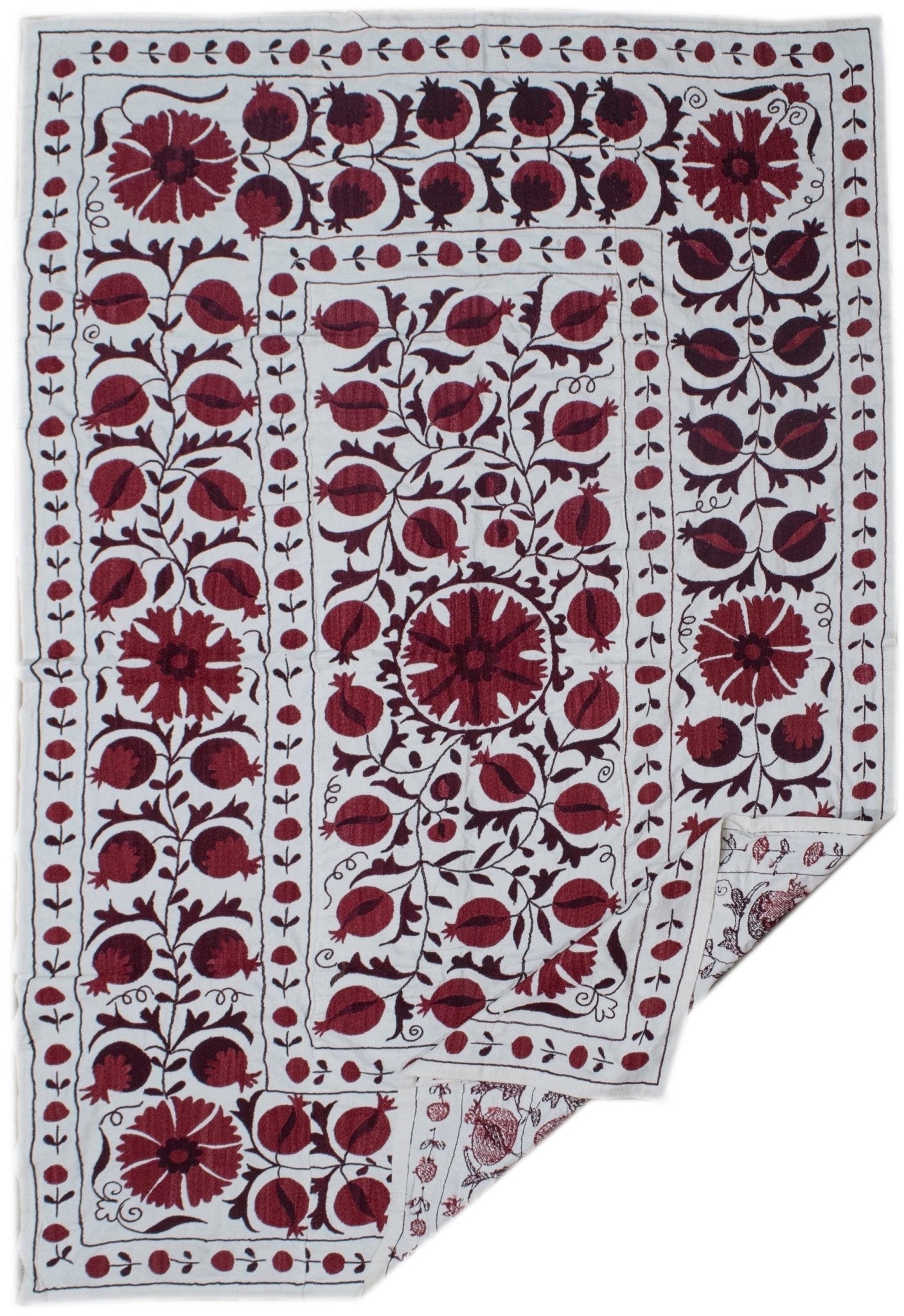 Hand-embroidered Uzbek suzani featuring deep red pomegranate and floral motifs on a white base.