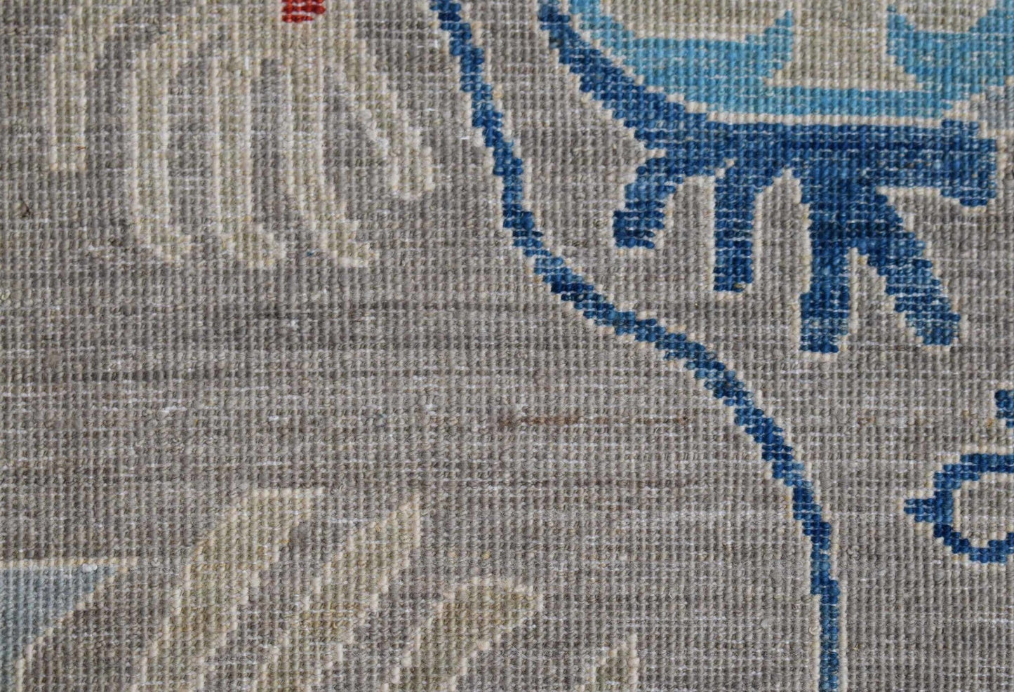 A close-up of a handwoven Afghan Chobi runner featuring blue floral patterns on a grey wool base.