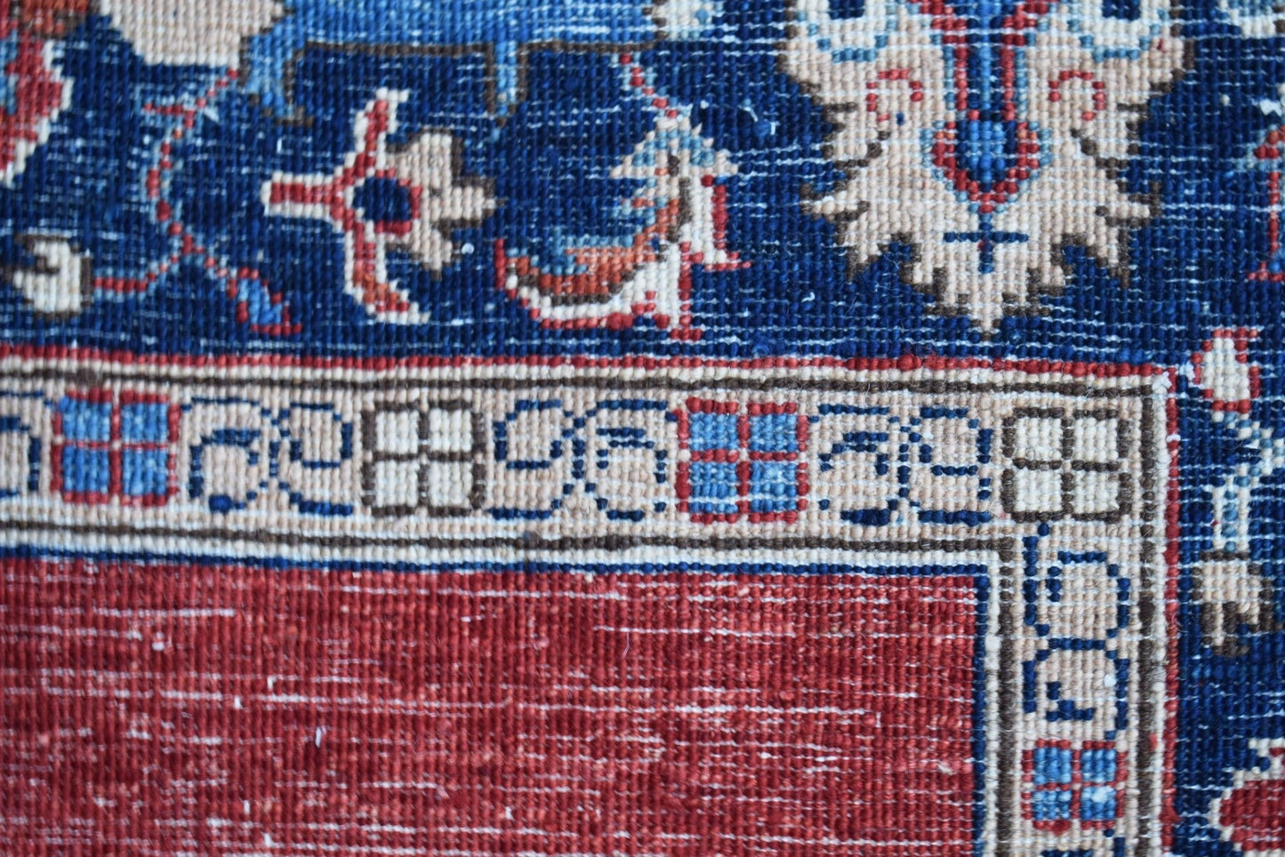 A close-up of a handwoven Afghan Chobi rug featuring a red field and a blue floral border.