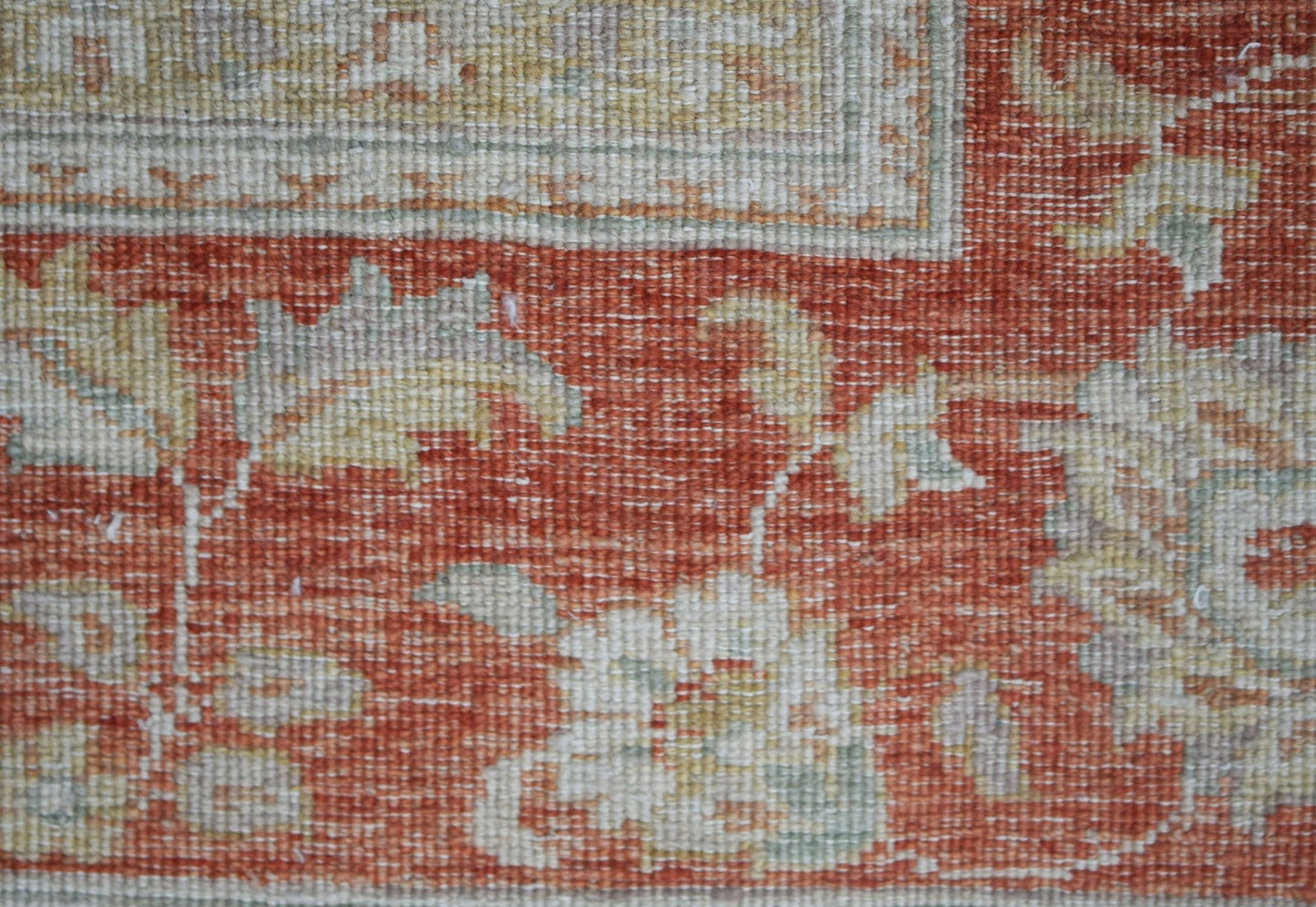 A close-up of a handwoven Afghan Chobi rug featuring floral patterns in muted tones on a red field.