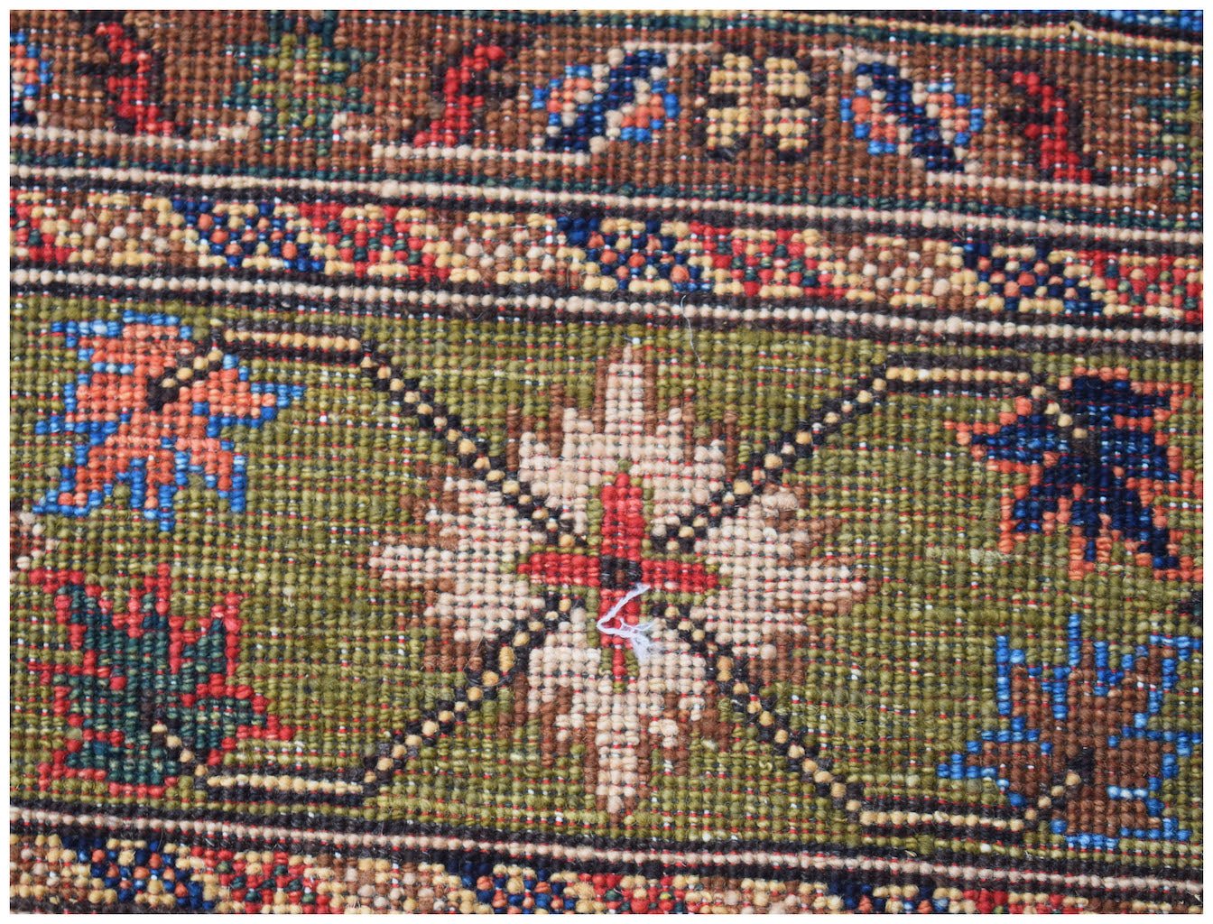 A close-up of an Afghan Chobi rug featuring a green field with a central floral motif and borders.