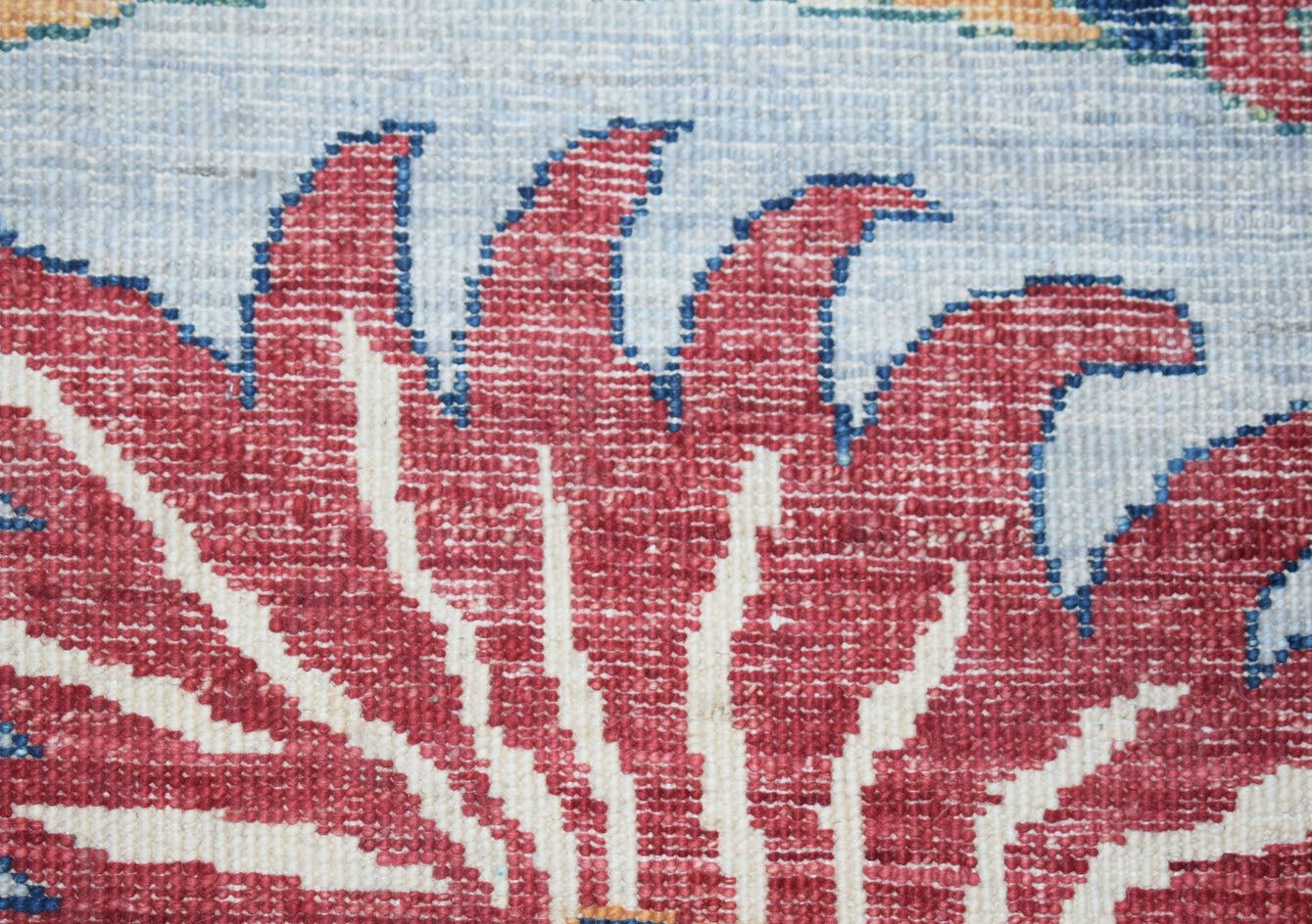 A close-up of an Afghan Chobi rug featuring a red floral motif with blue outlines on a light base.