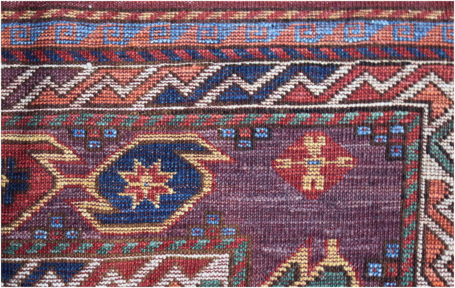 A close-up of a handwoven Afghan Herati rug featuring intricate geometric patterns in wool.