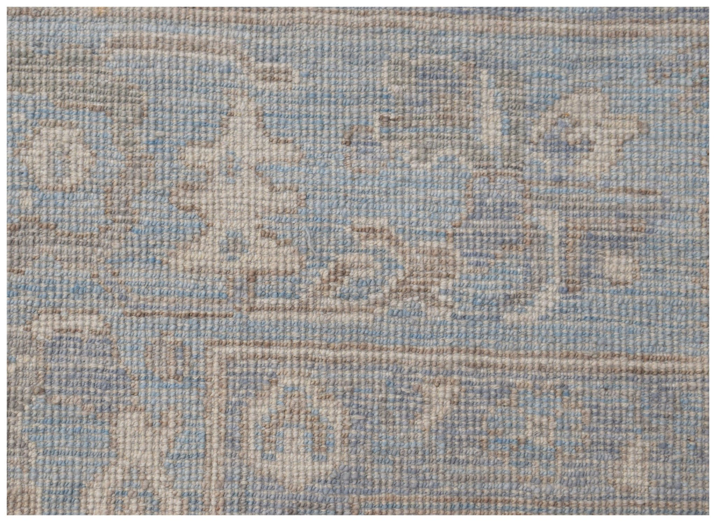 A handmade wool rug featuring a traditional Oushak pattern in soft blue and beige tones.