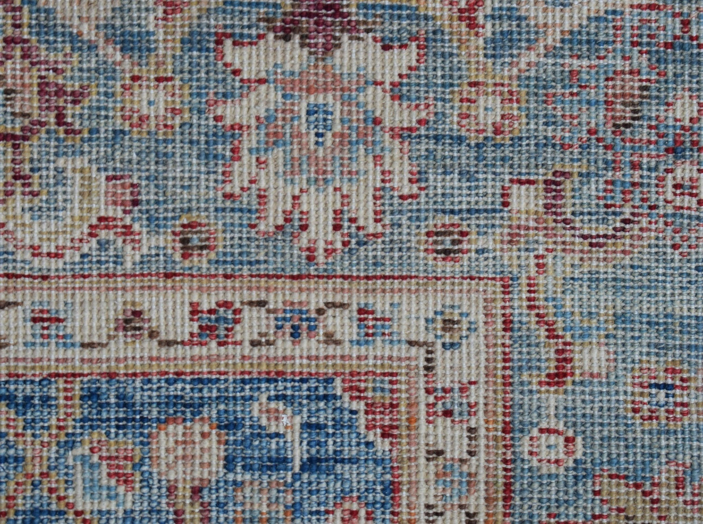 A close-up of a handwoven Afghan Chobi rug featuring intricate floral patterns in blue and red.