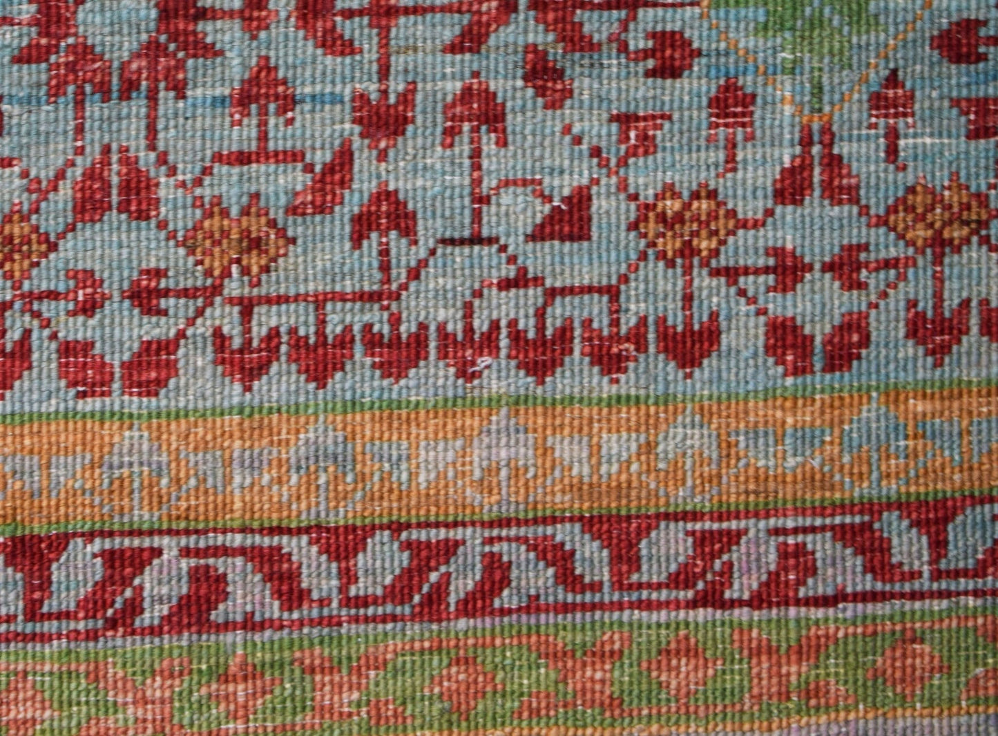 A close-up of an Afghan Chobi rug featuring intricate red floral patterns on a light blue field.