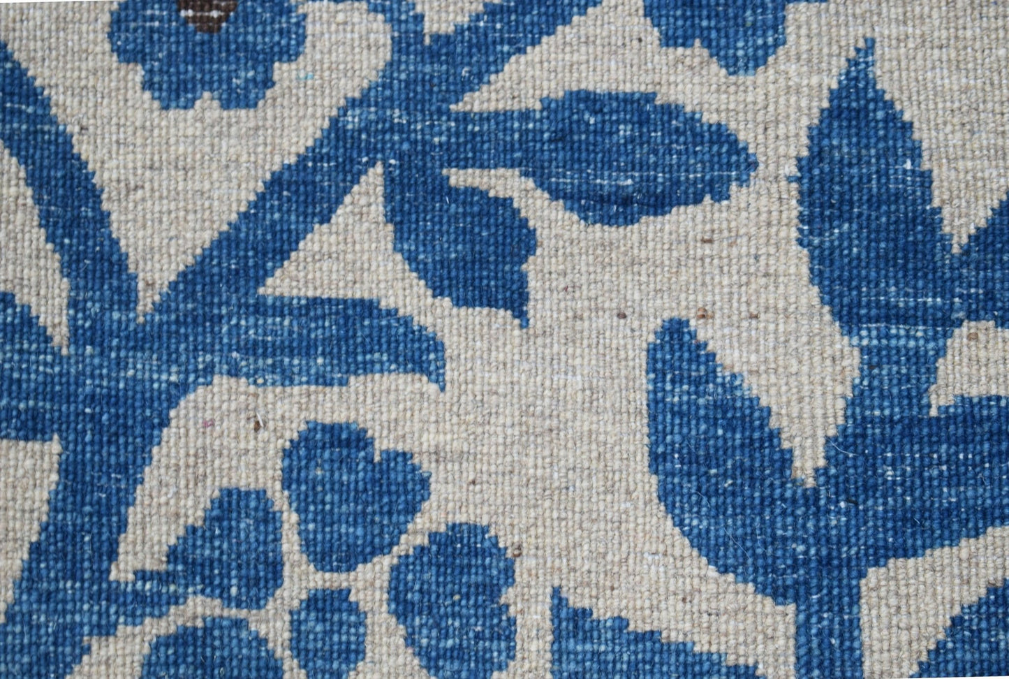 A close-up of a handwoven Afghan Chobi rug featuring a blue floral pattern on a cream background.