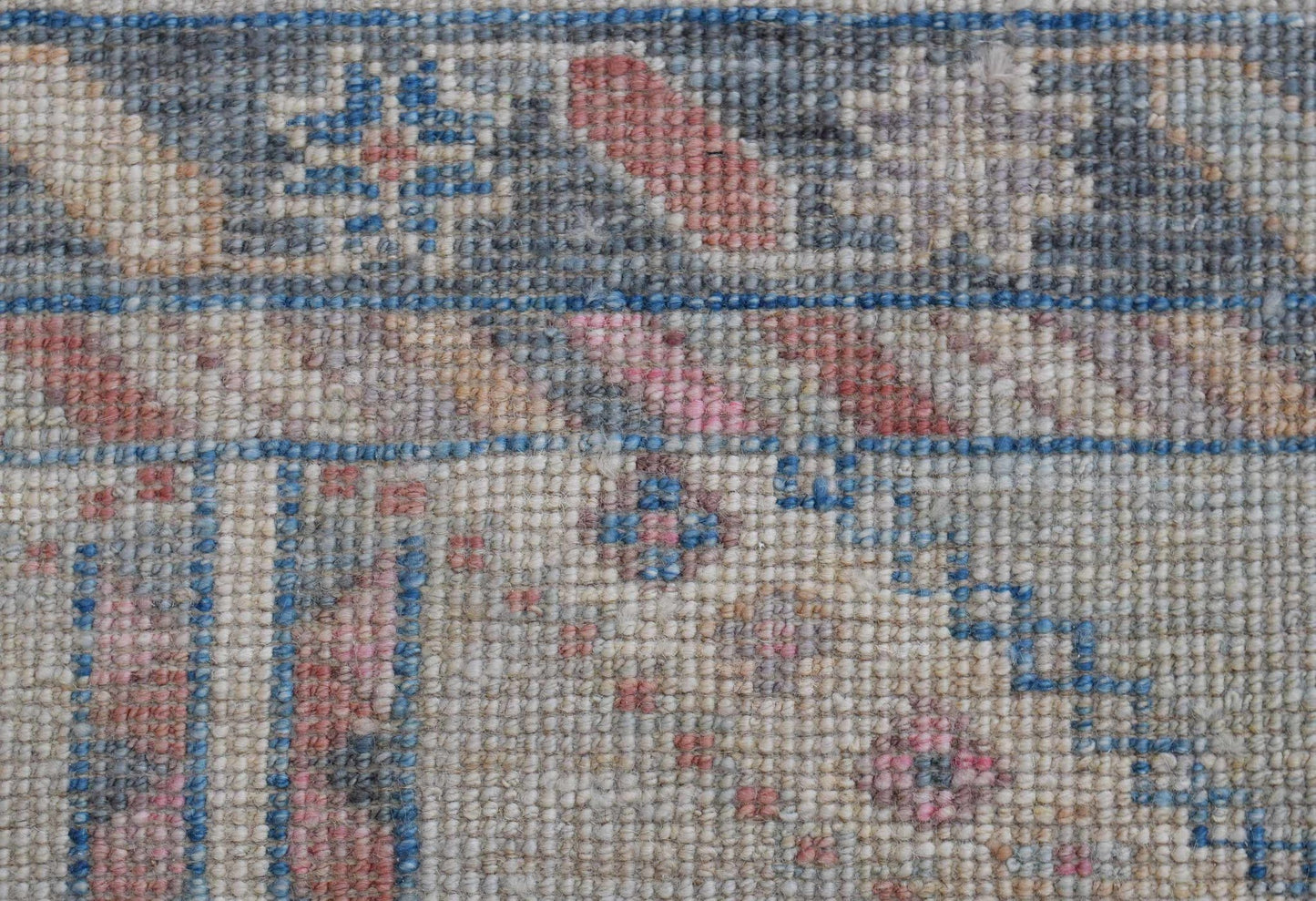 A close-up of a handwoven wool runner rug featuring a transitional floral pattern in muted tones.