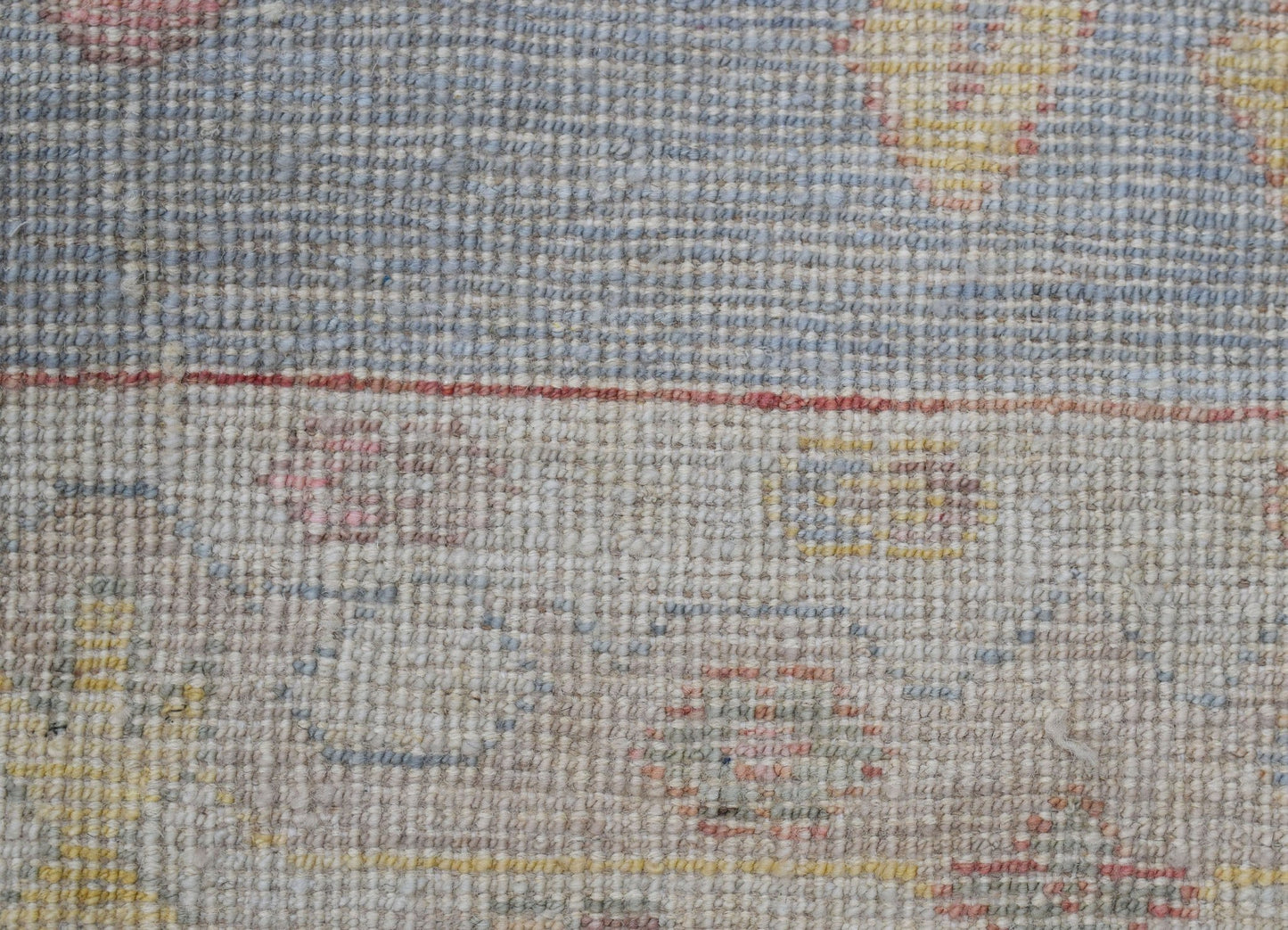 A close-up of a handwoven wool runner featuring a transitional floral pattern in muted tones.