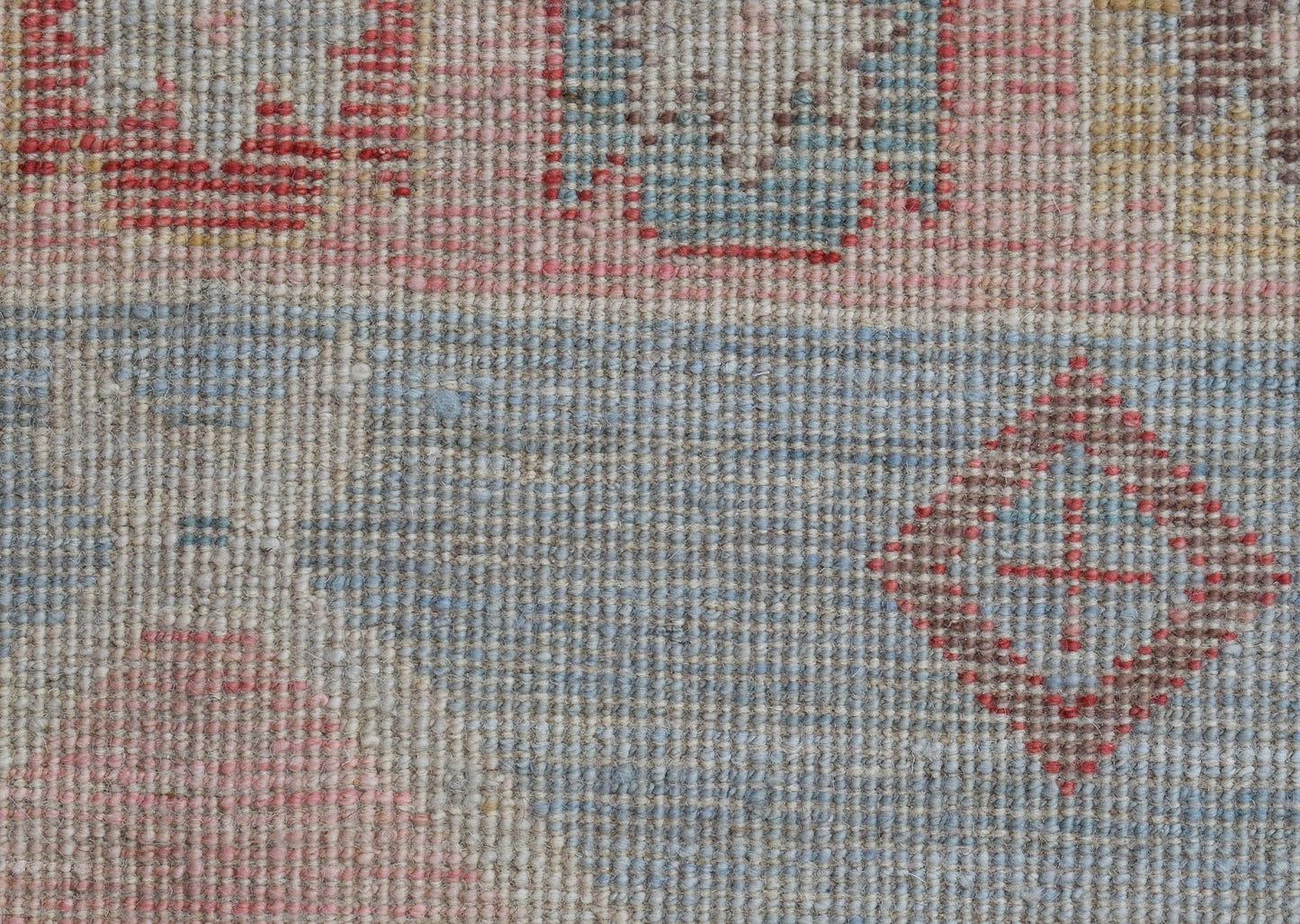 A close-up of a handwoven wool runner featuring a transitional pattern in soft blue and red tones.