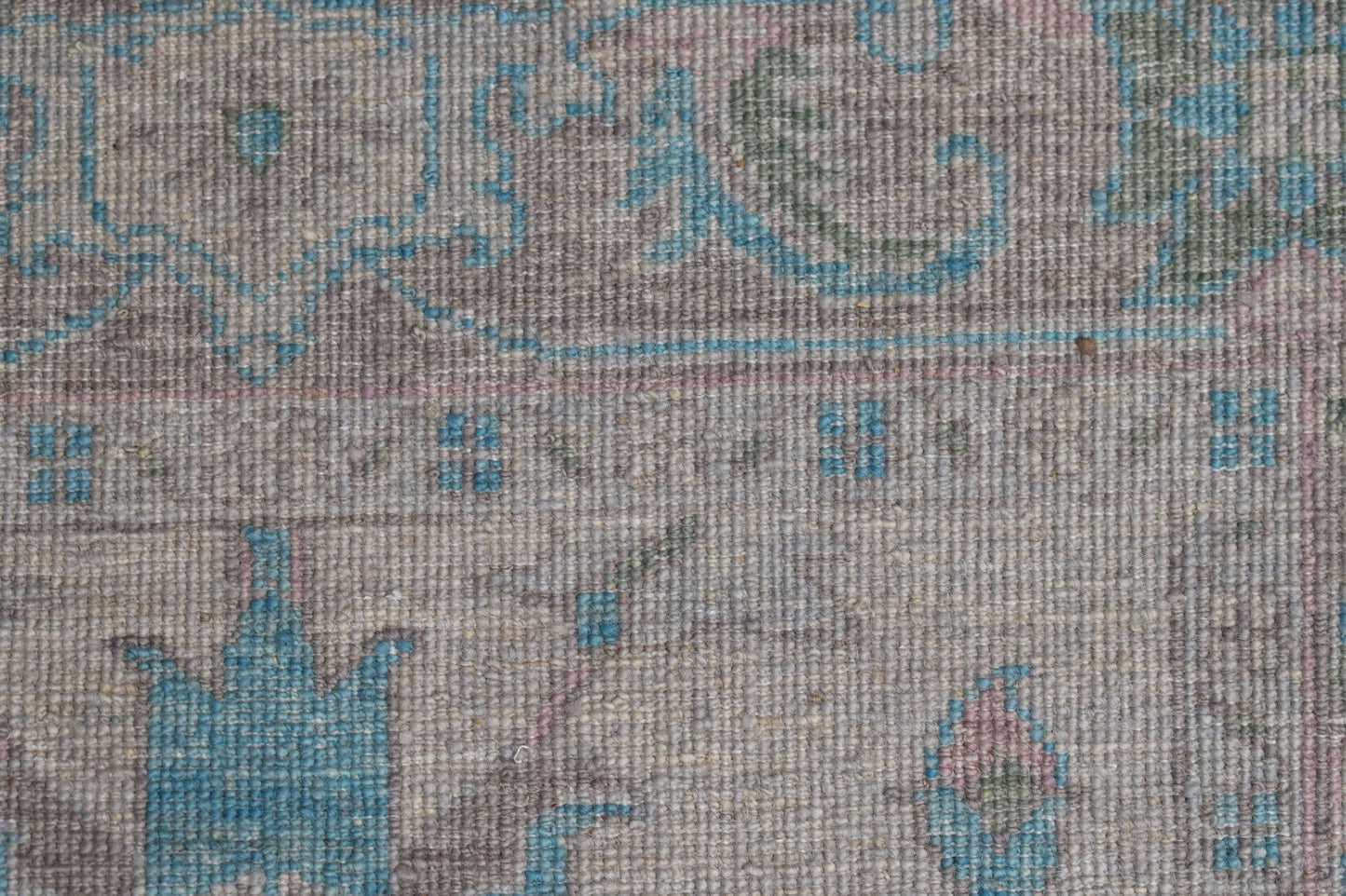 A close-up of a handwoven wool runner featuring a transitional floral pattern in blue and grey.
