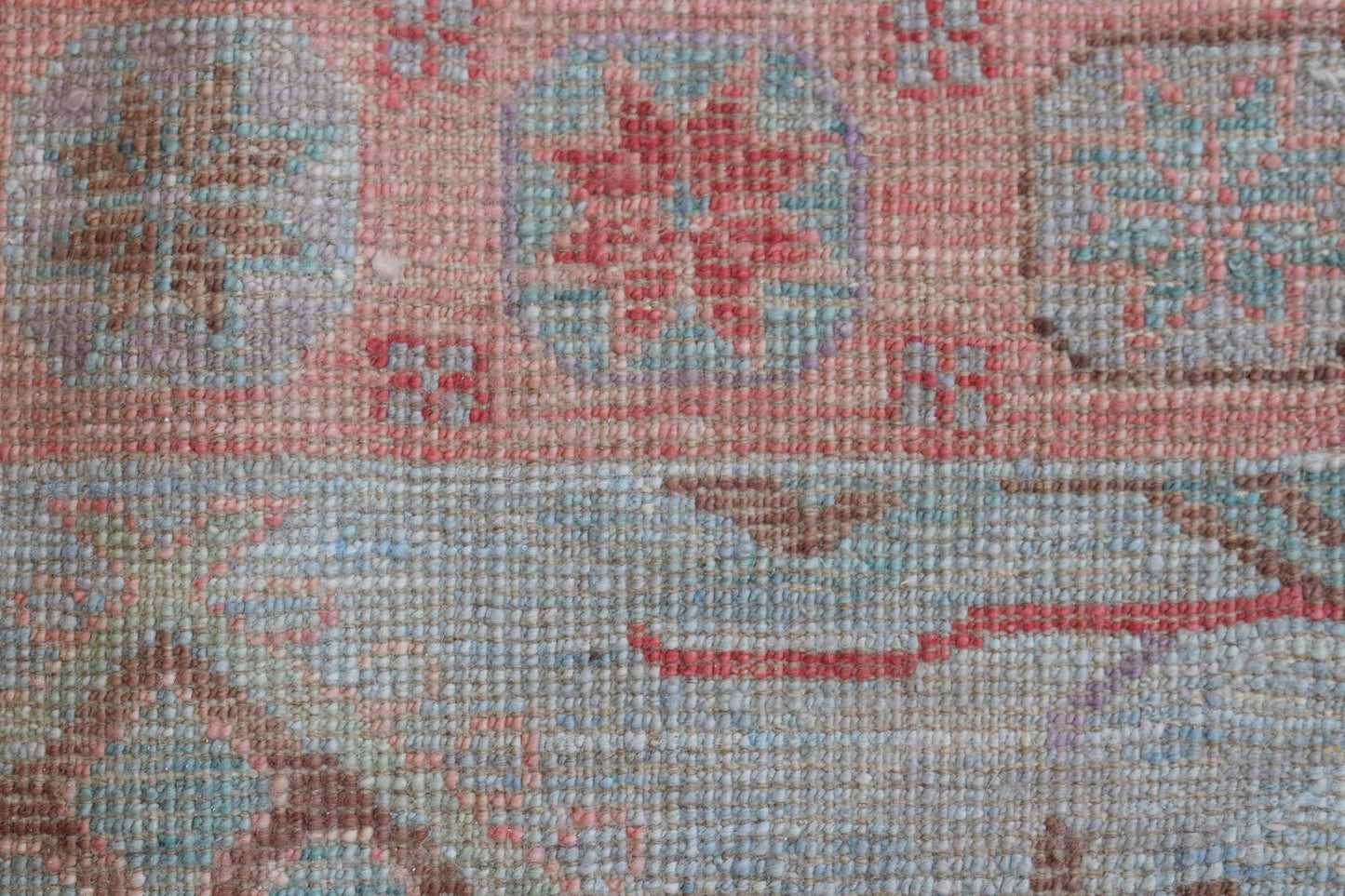 A close-up of a handwoven wool runner rug featuring a transitional floral pattern in soft tones.