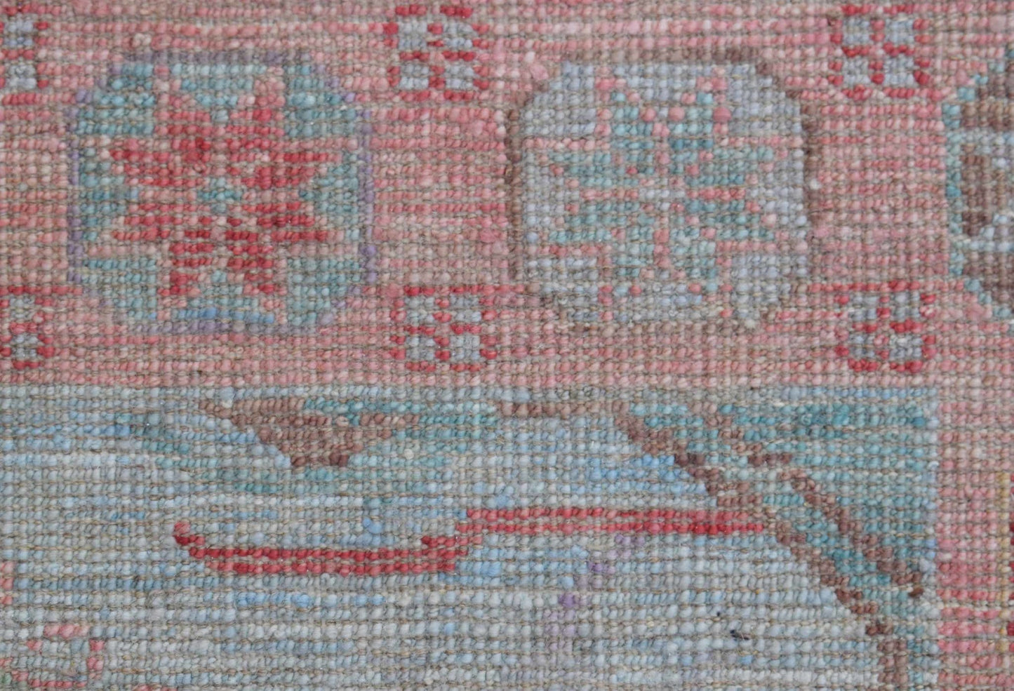 A close-up of a handwoven wool runner featuring a transitional floral pattern in pink and blue.