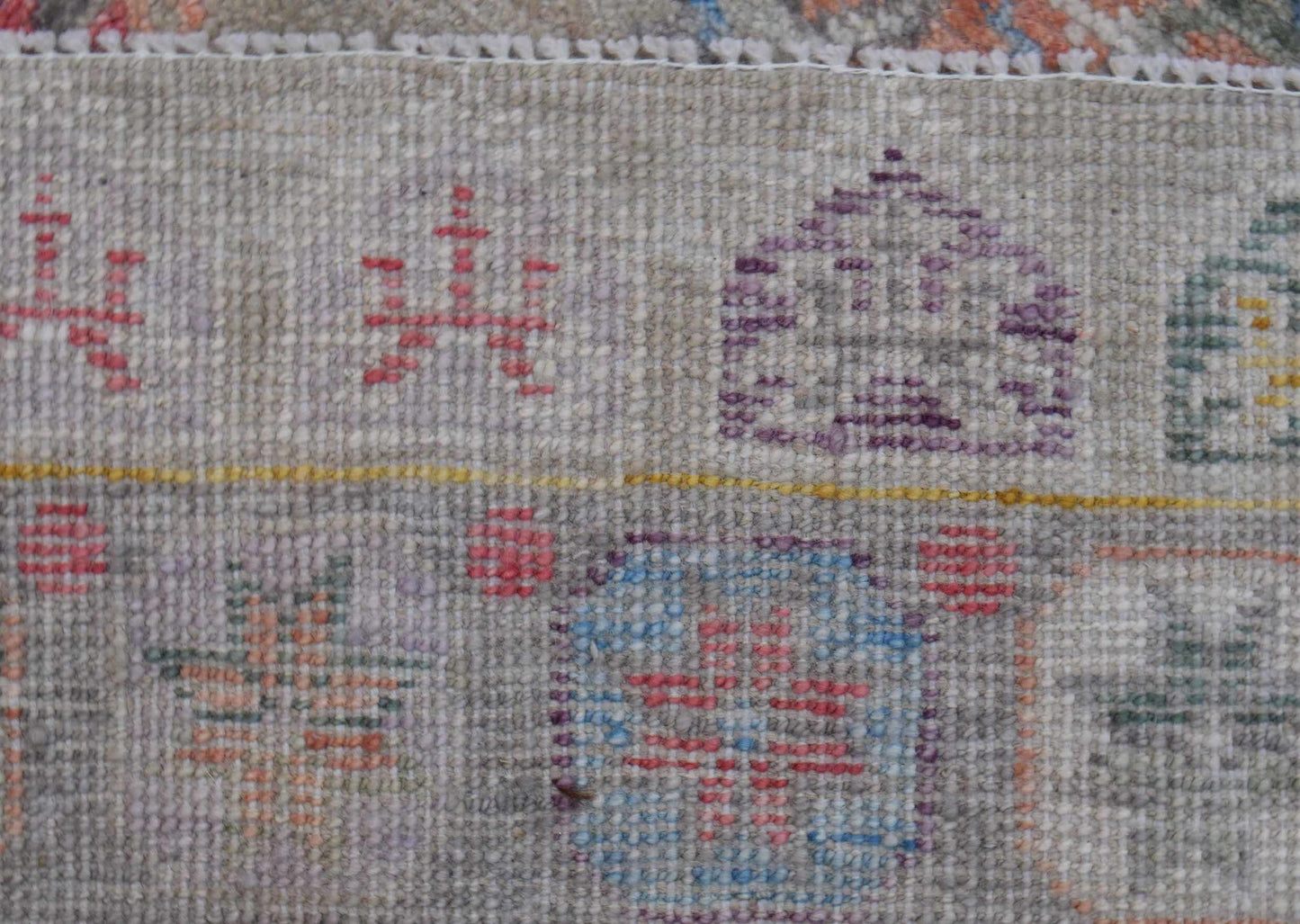 A close-up view of a handwoven wool rug featuring geometric patterns in muted, earthy tones.