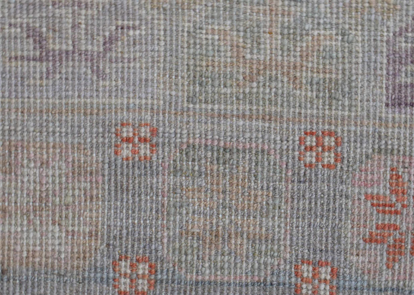 A close-up of a handwoven wool rug featuring a muted, transitional pattern with small orange motifs.