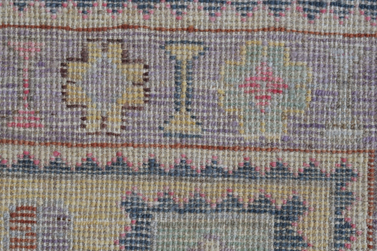 A close-up of a handwoven Oushak rug featuring geometric patterns in muted pastel tones.
