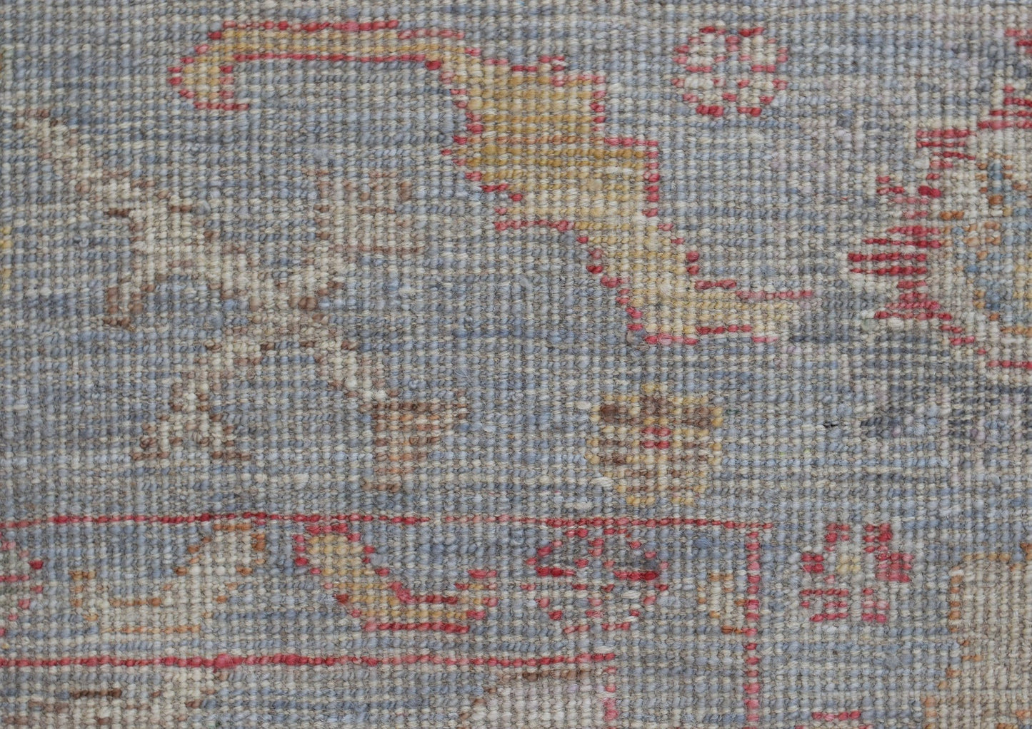 A close-up of a handwoven Oushak rug featuring a floral pattern in muted blue, red, and gold tones.