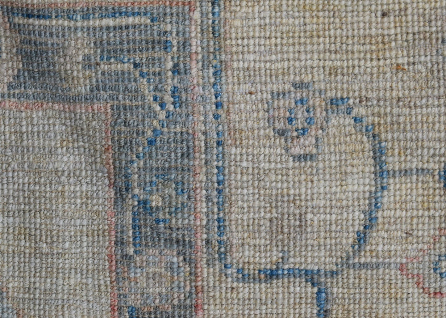A close-up view of a handwoven wool rug featuring a blue floral pattern on a neutral background.