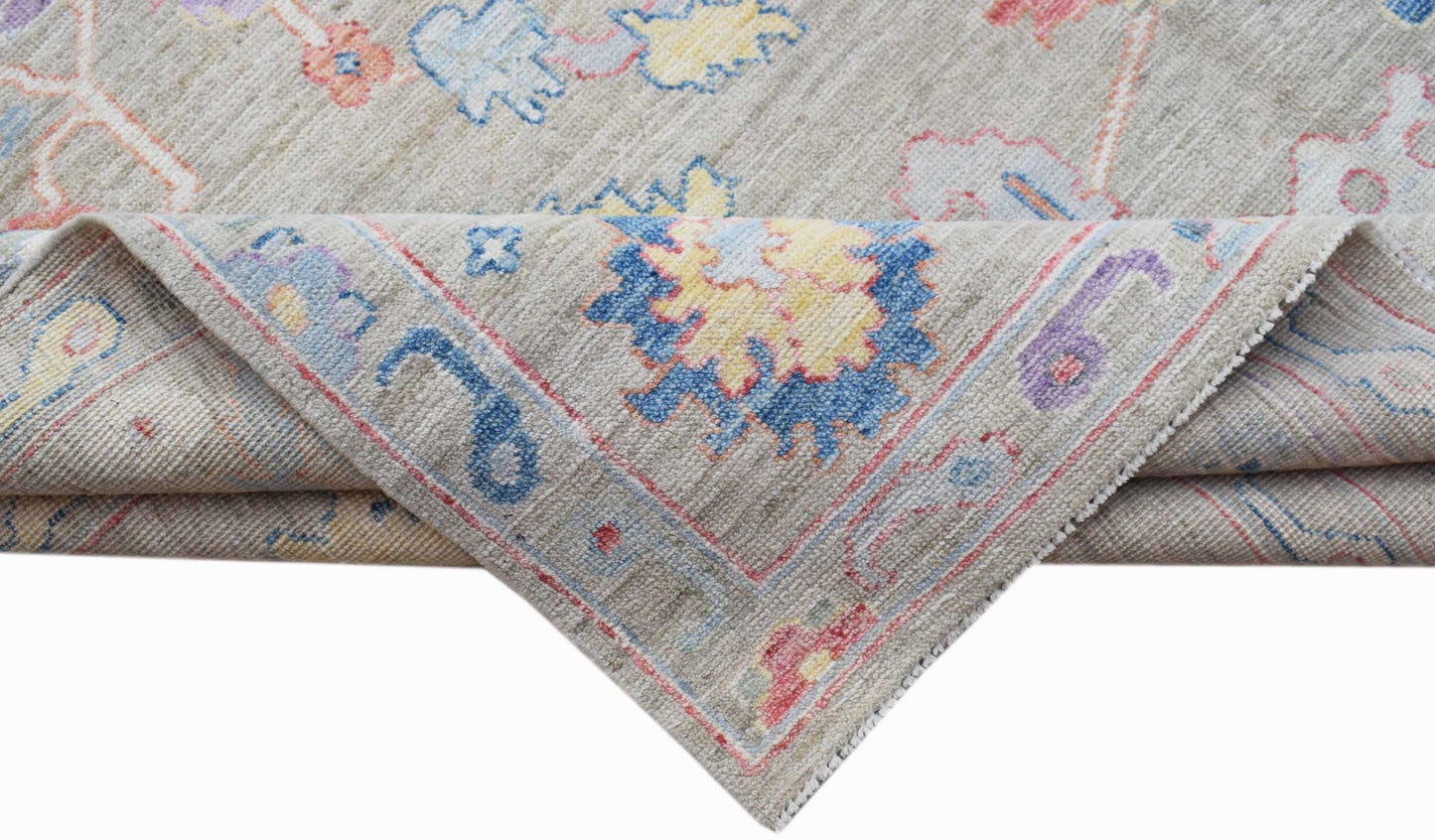A handwoven transitional Oushak rug with a floral pattern in blue, yellow, and pink on a beige base.