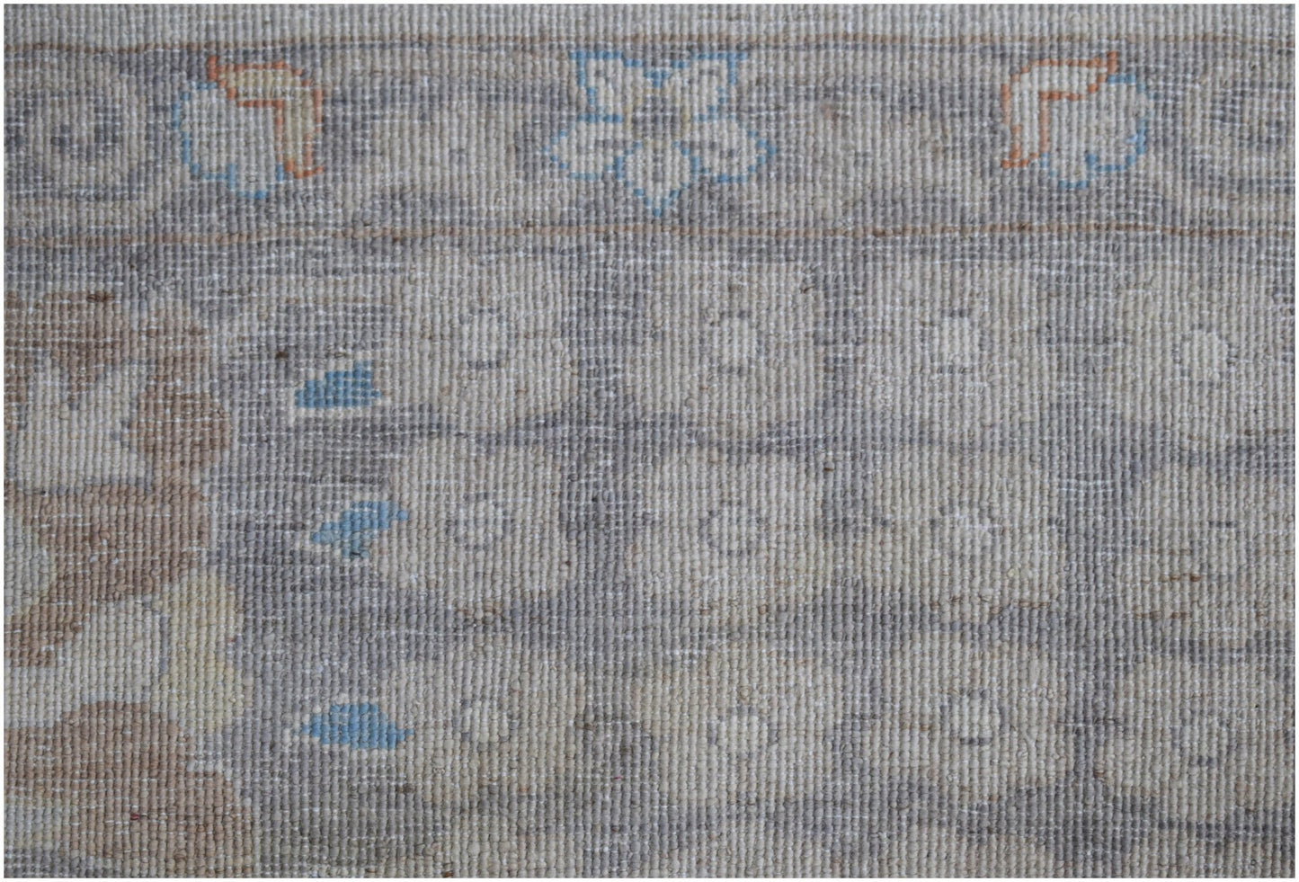 A handwoven transitional Oushak rug featuring a floral pattern in soft grey, blue, and tan tones.