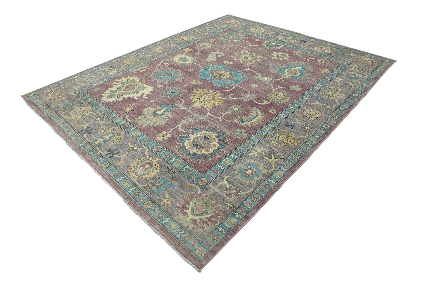 A transitional Oushak rug featuring a floral pattern in muted tones on a mauve background.