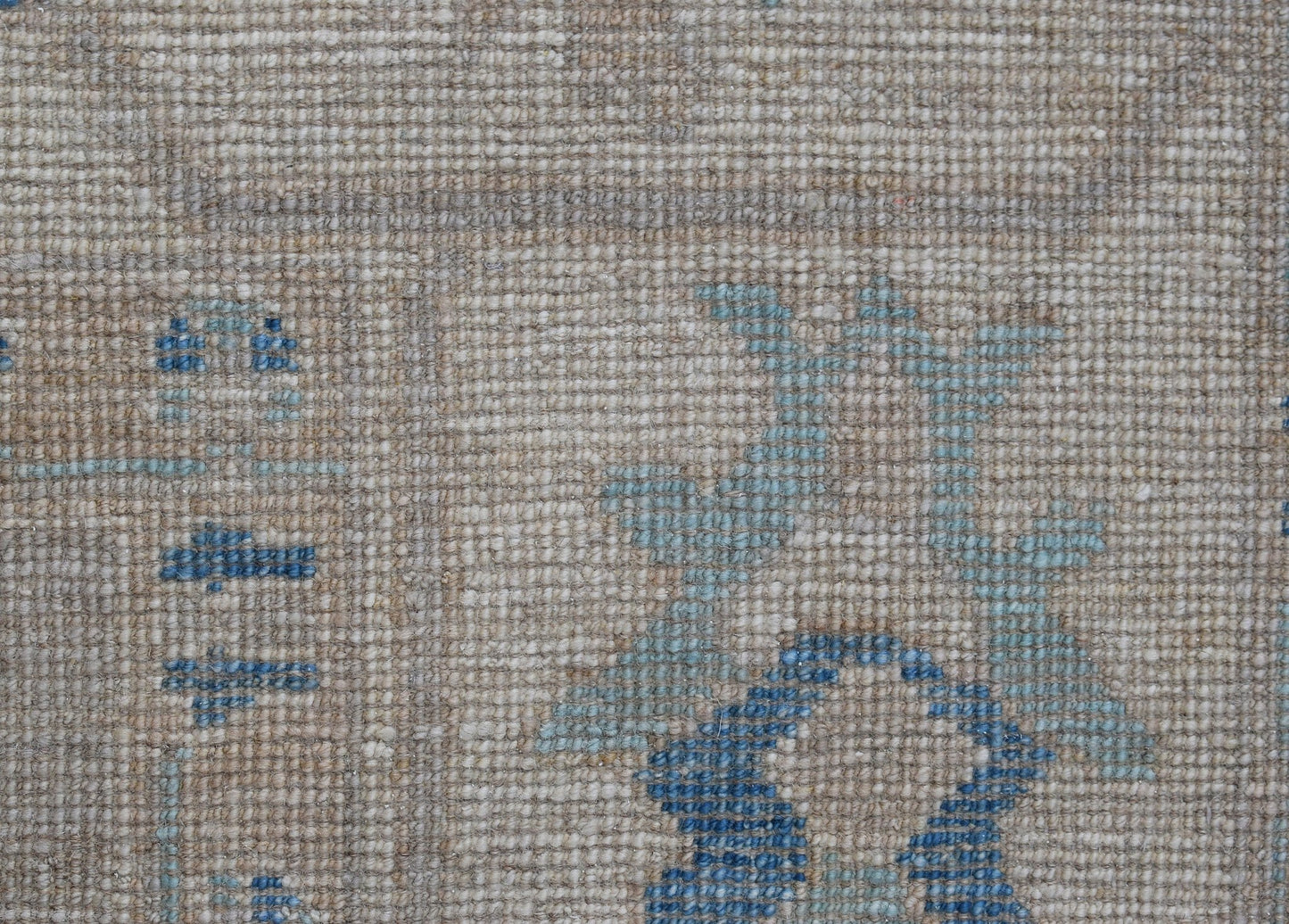 A close-up of a handwoven transitional Oushak rug featuring a floral pattern in blue on a beige wool background.