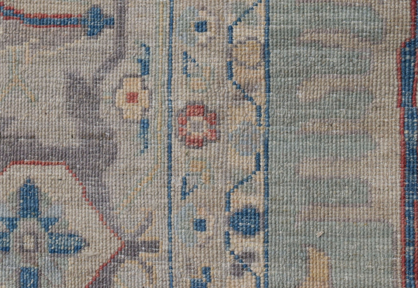 A close-up of a handwoven Oushak rug featuring a floral pattern in blue, red, and beige tones.