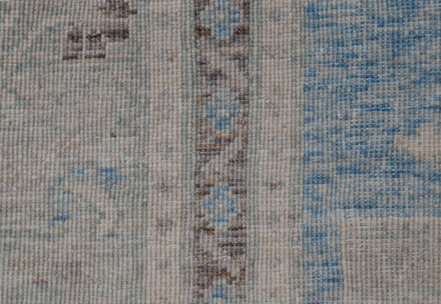 A close-up of a handwoven wool rug featuring a transitional pattern in blue, beige, and brown.