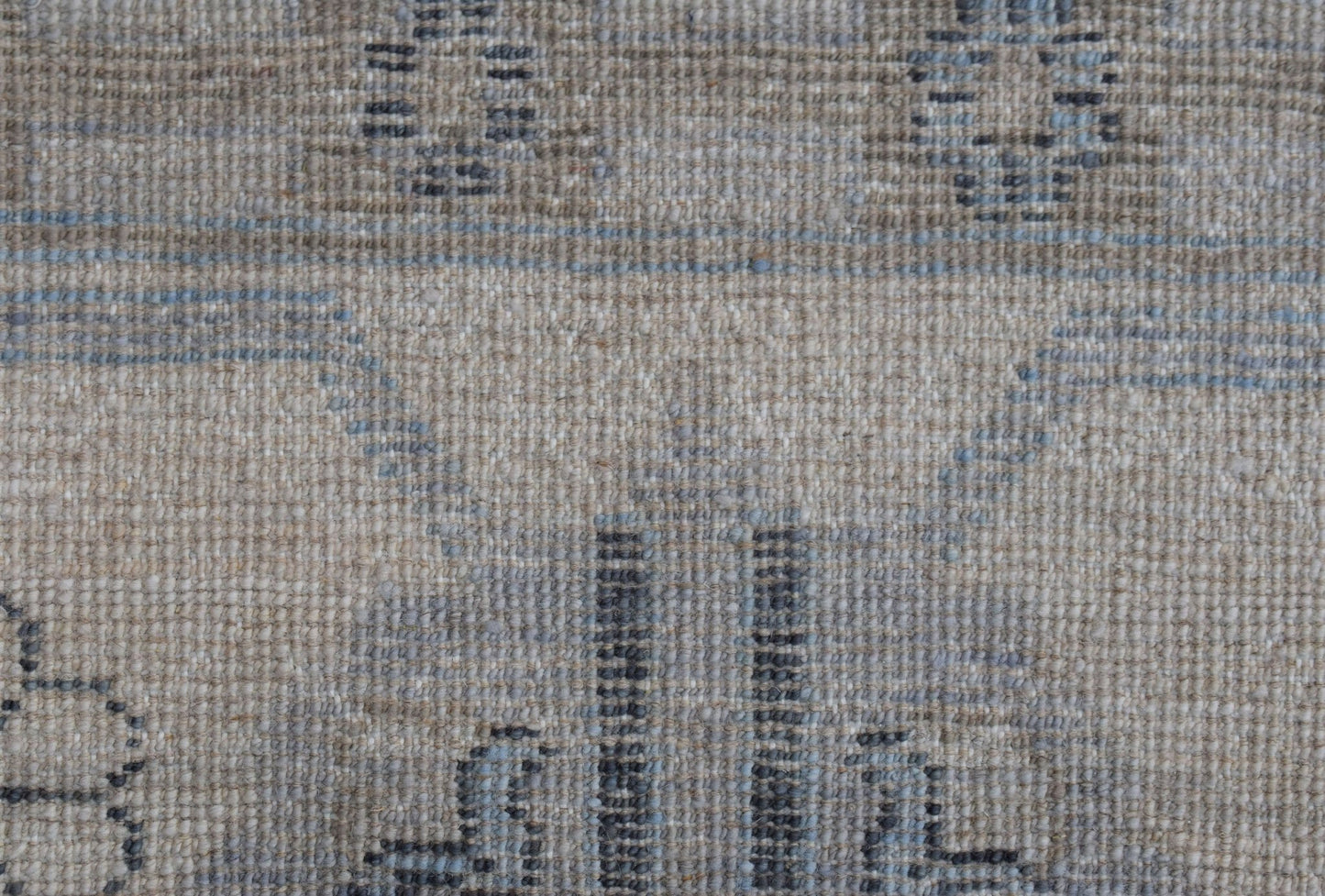 A close-up of a handwoven wool rug featuring a transitional pattern in soft blue and beige tones.