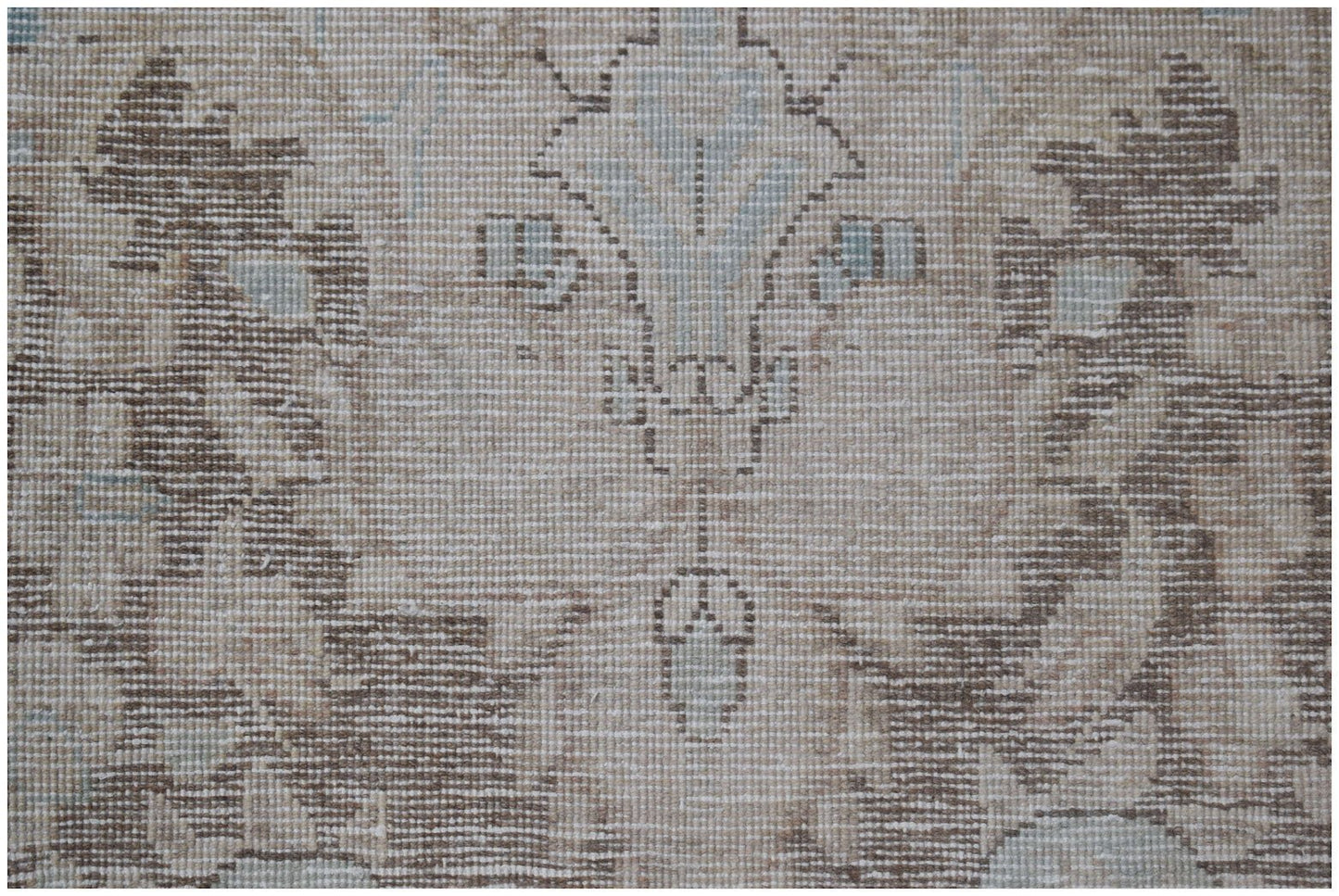 A close-up of a vintage Persian Kerman rug featuring intricate floral patterns in neutral tones.