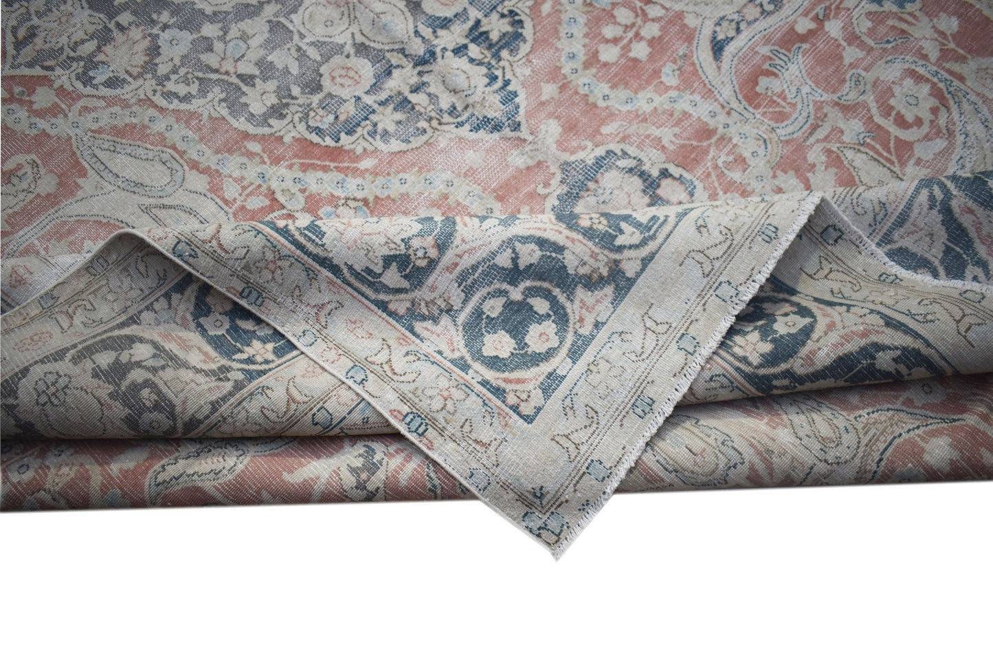 A vintage Persian Kerman rug featuring a faded floral medallion pattern in blue and coral tones.