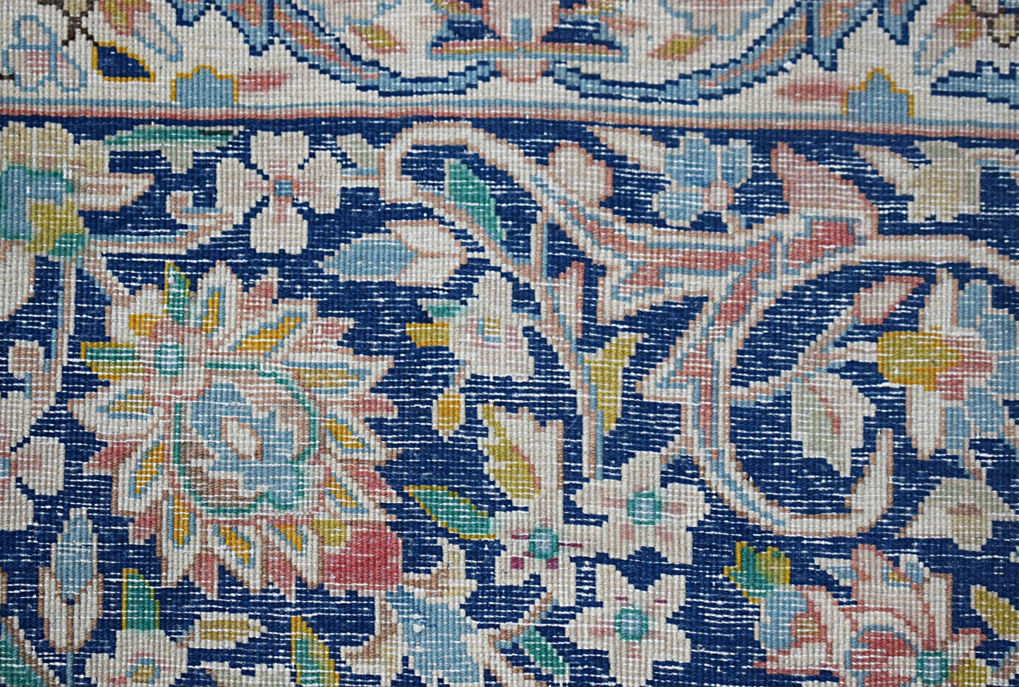 A close-up of a vintage Persian Kerman rug featuring intricate floral patterns on a blue field.