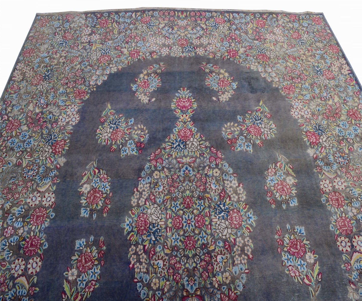 A vintage Persian Kerman rug featuring a central floral medallion on a blue field.