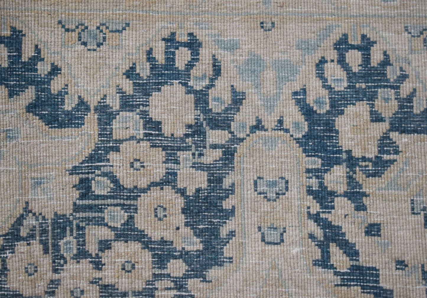 A close-up of a vintage Persian Kerman rug featuring intricate blue floral patterns on a beige base.